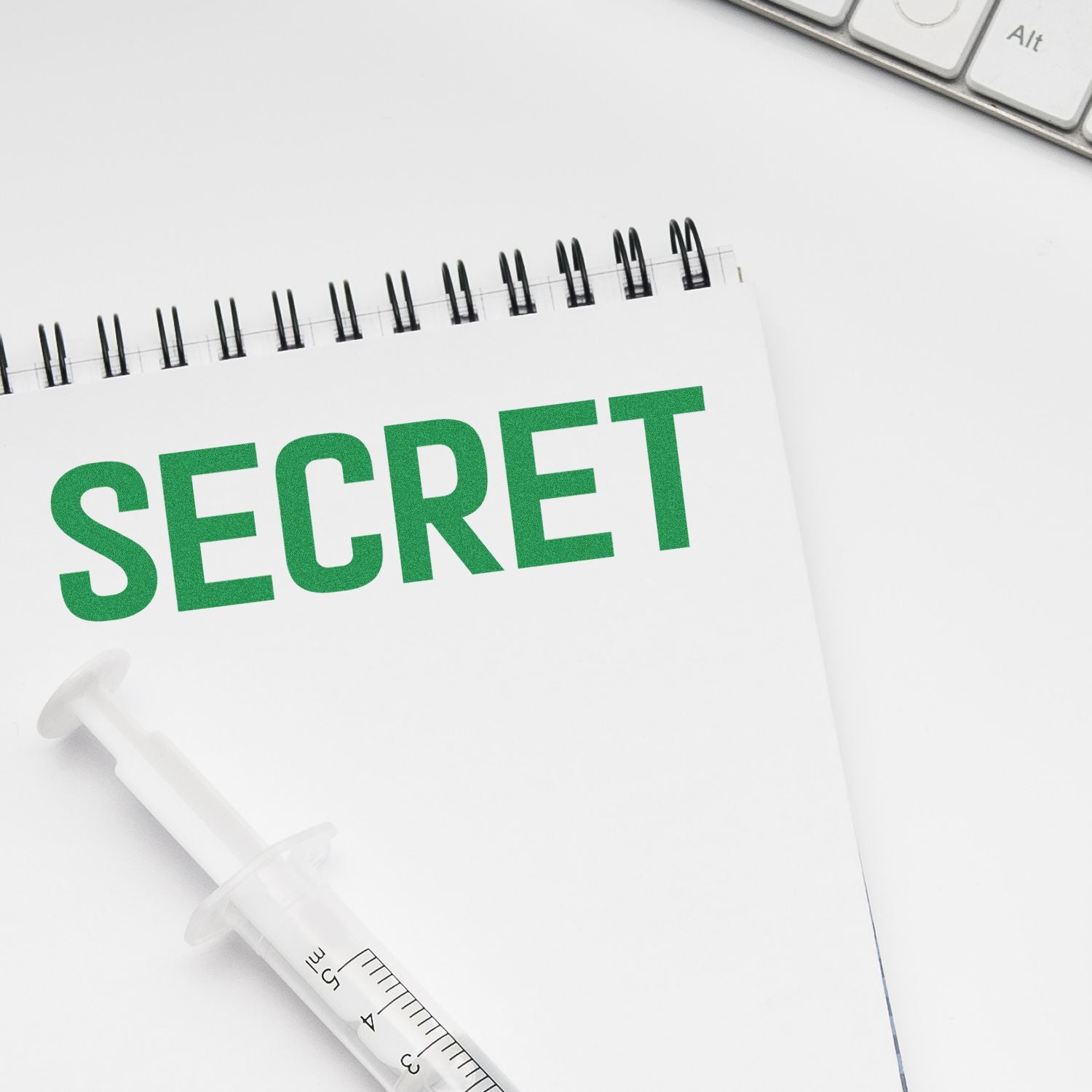 Notebook with SECRET text, syringe, and keyboard on a white desk, symbolizing confidential medical or business information.