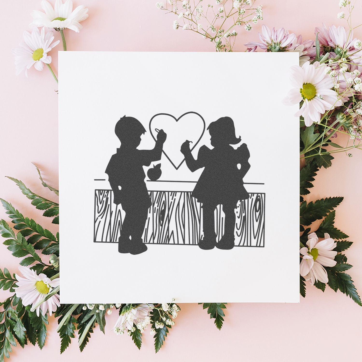 Floral flat lay with a white card featuring children drawing a heart silhouette, romantic Valentines Day craft design.