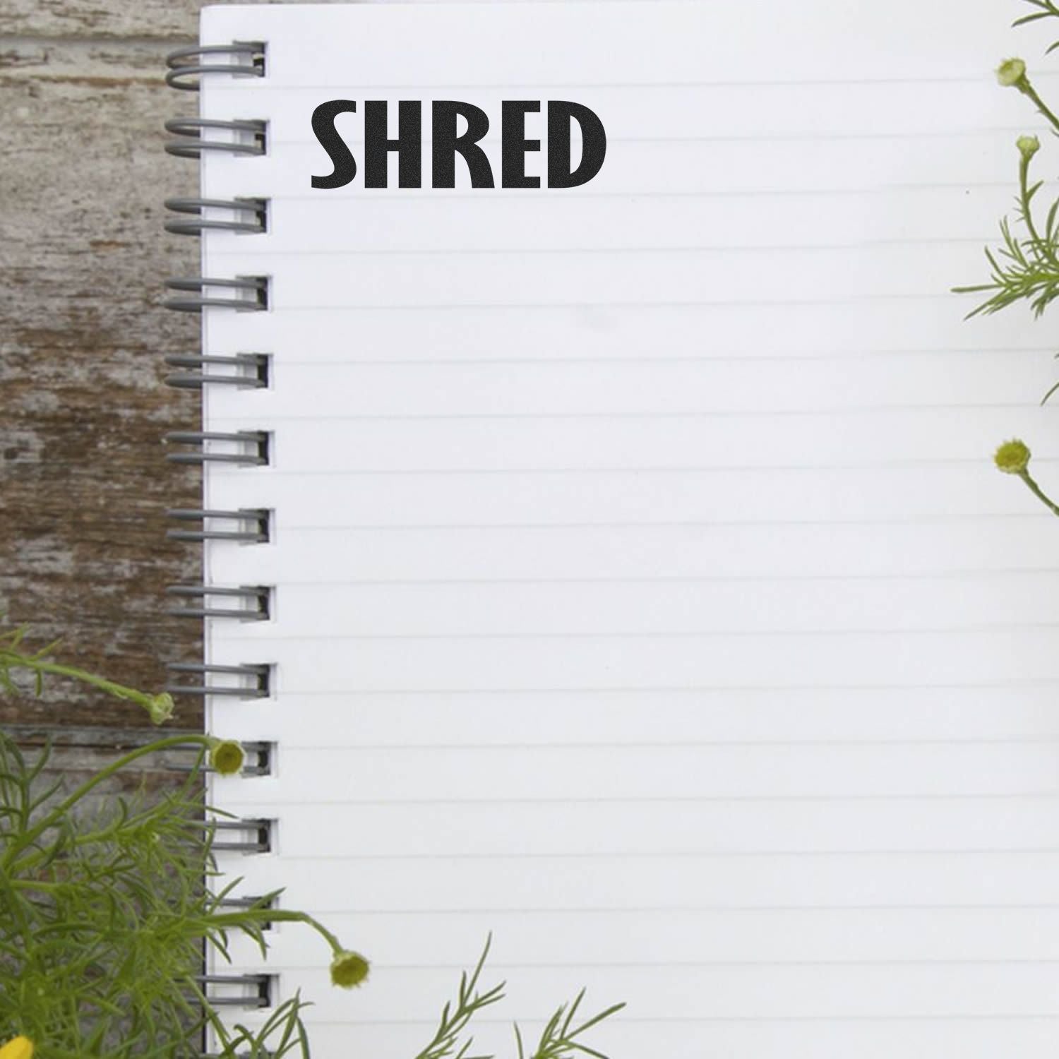 Blank spiral notebook page with bold SHRED text on rustic wood background and green foliage accents.