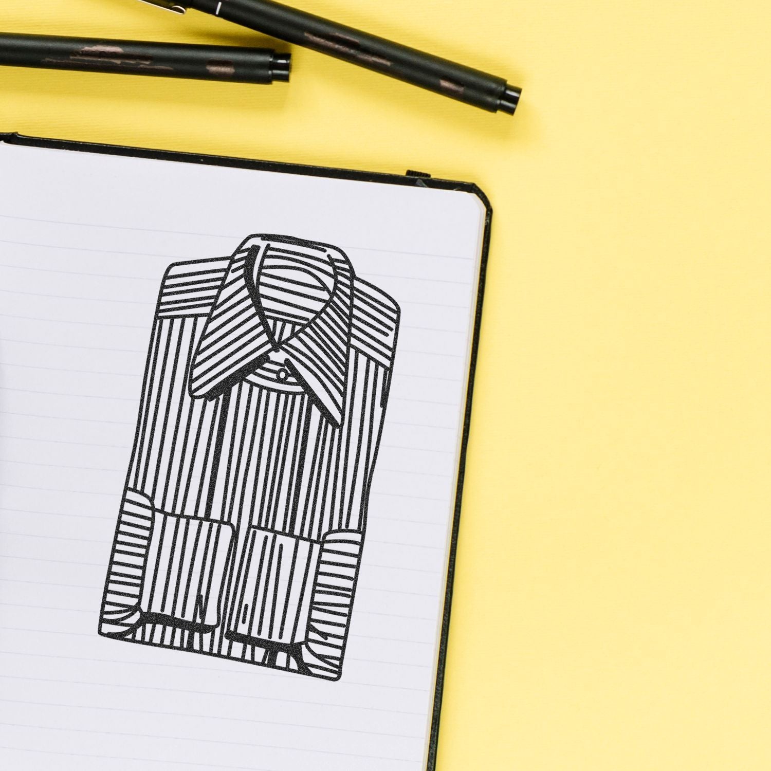 Open notebook with abstract black line drawing, pens, and yellow background, creative stationery concept.