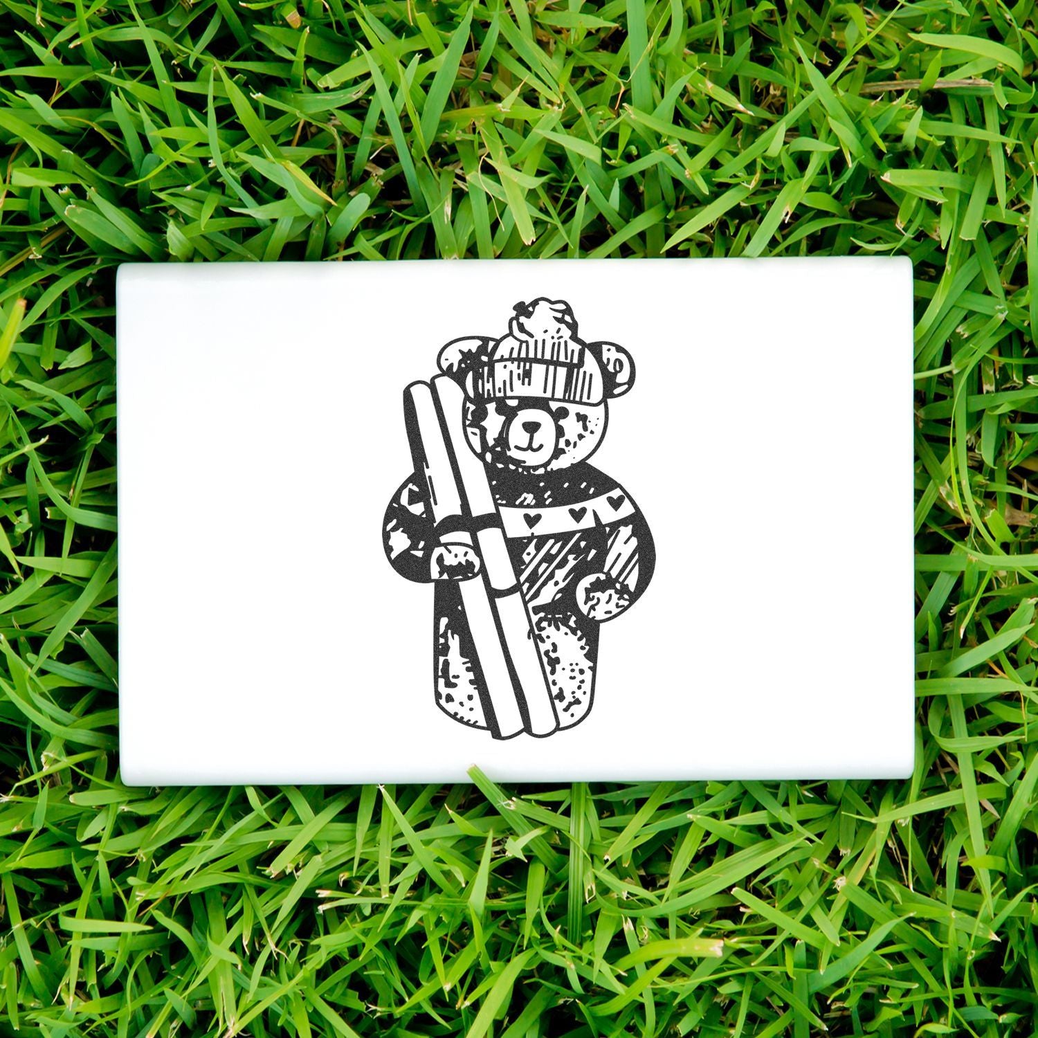 White laptop with cute black teddy bear graphic on green grass background