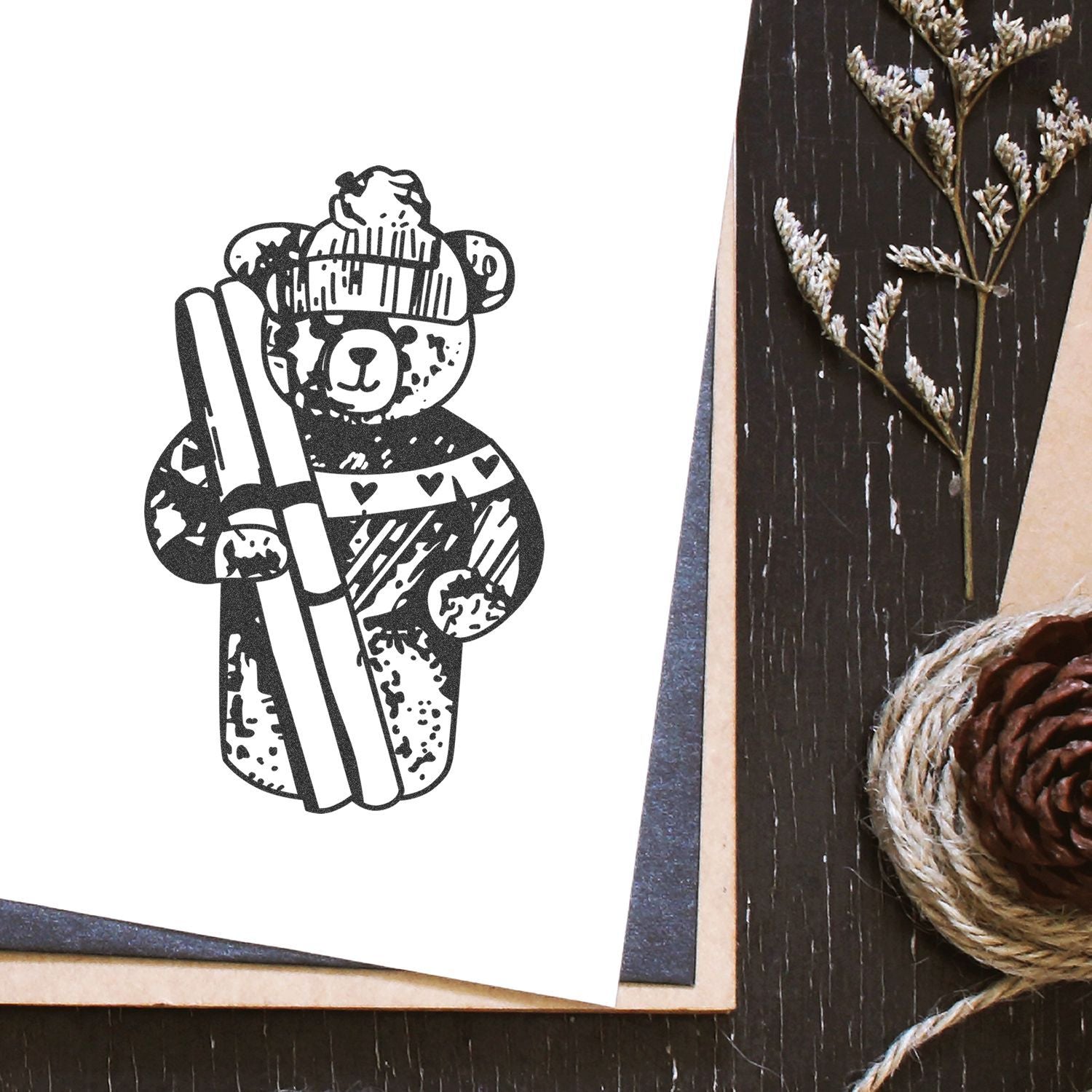Cute black and white bear illustration on a handmade greeting card with rustic pinecone and twine decor on a wooden table.