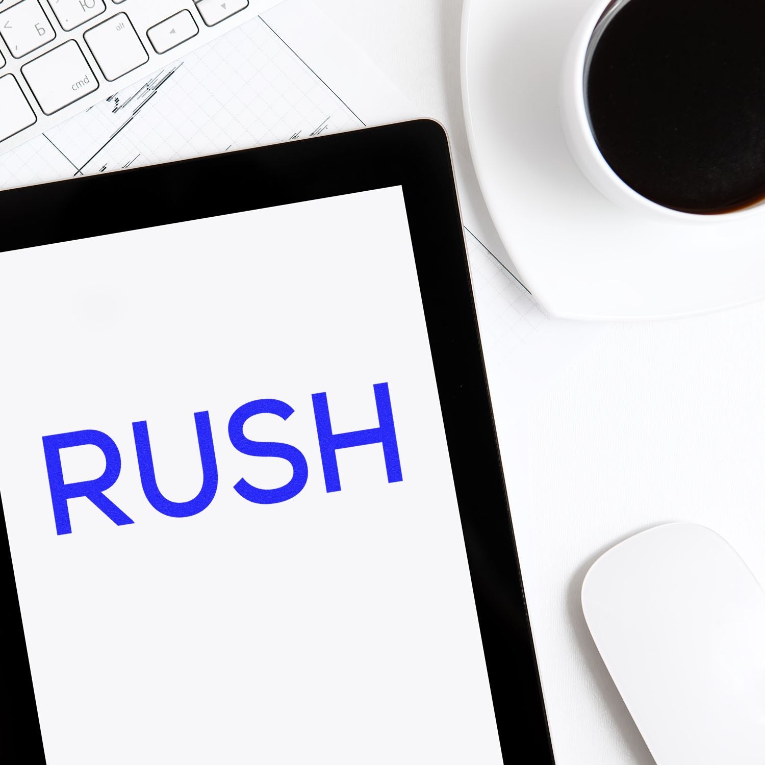 Tablet screen reads RUSH on an office desk with keyboard and coffee, emphasizing urgent turnaround for projects.