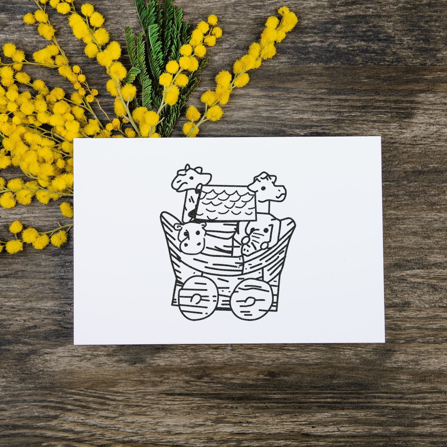 Noahs Ark illustration on white card with yellow mimosa flowers on rustic wooden background