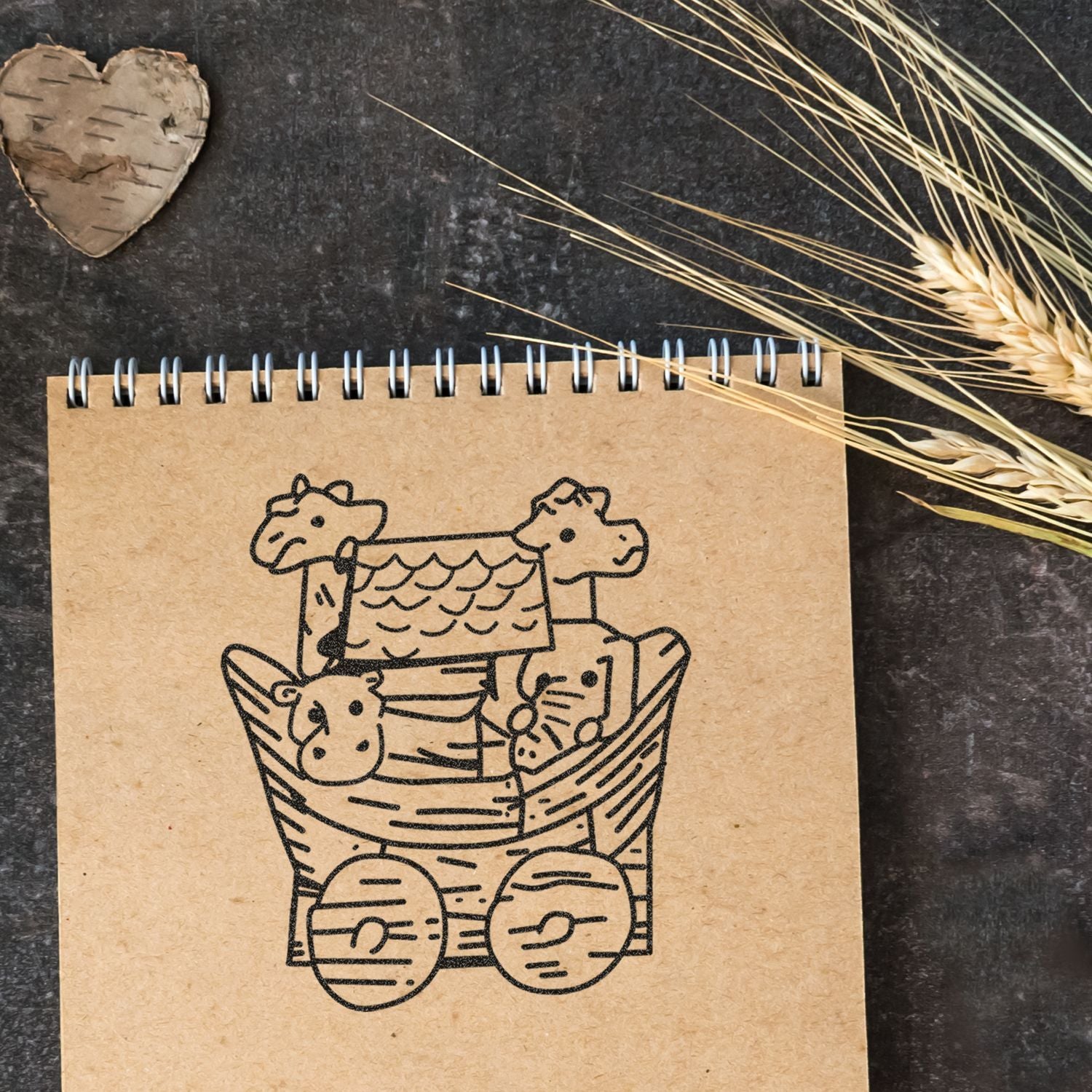 Rustic kraft spiral notebook with cute teddy bear basket illustration, dried wheat decor, and wooden heart on dark background.
