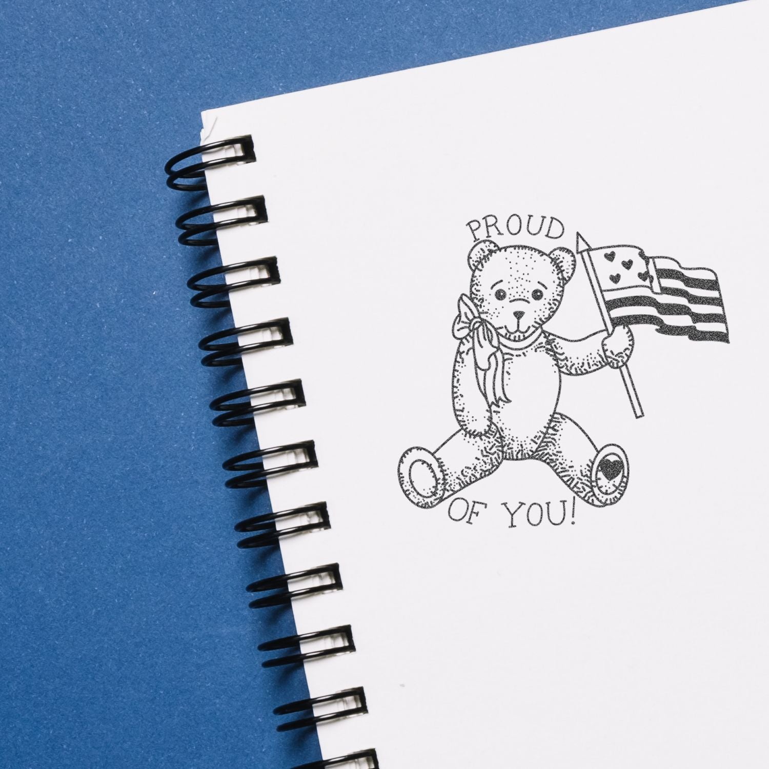 Spiral notebook with teddy bear holding a pride flag and Proud of You text on a blue background, inspirational LGBTQ+ design.