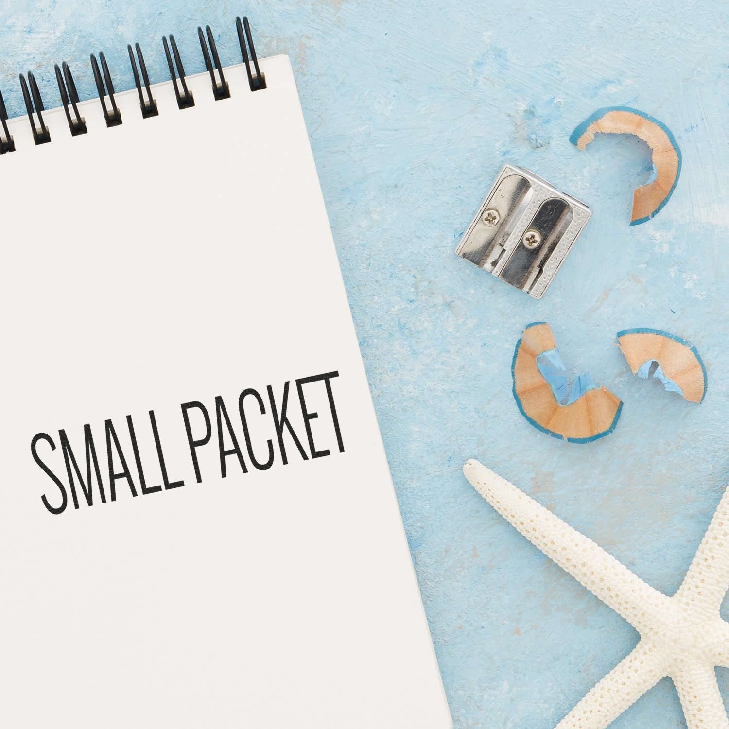 Small packet notebook with pencil sharpener and starfish on a blue background, creative summer stationery flat lay.