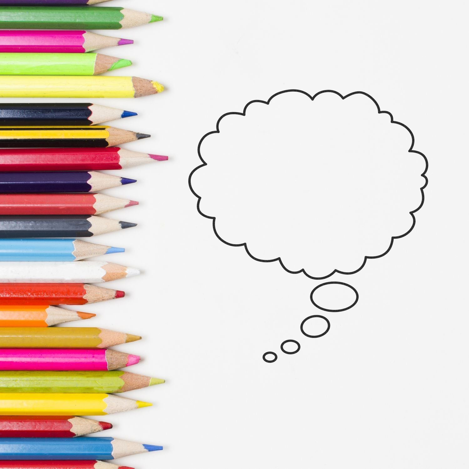 Colorful pencils beside blank thought bubble outline on white background, creative education concept.