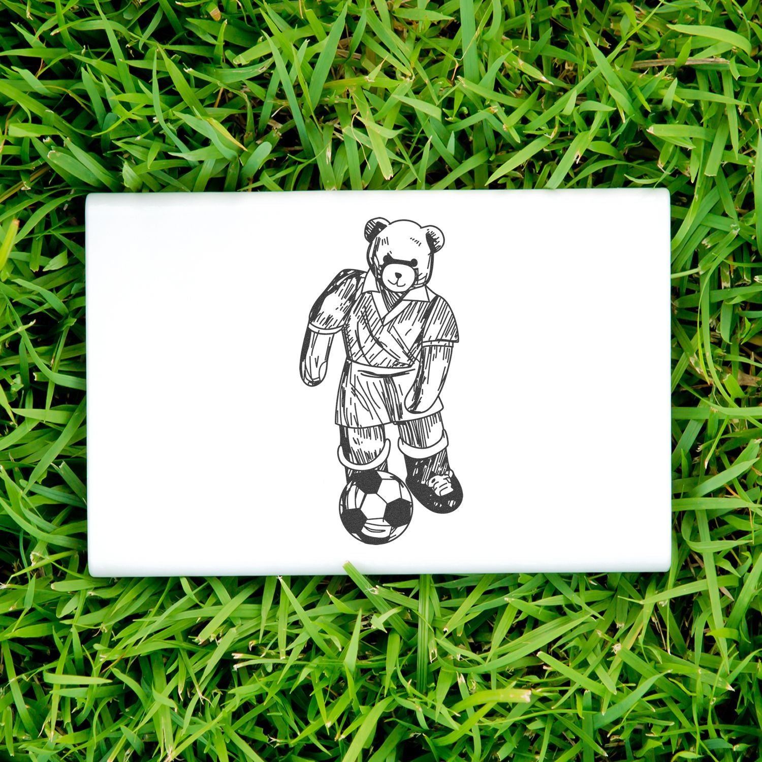 Teddy bear soccer player illustration on a white tile placed on green grass.