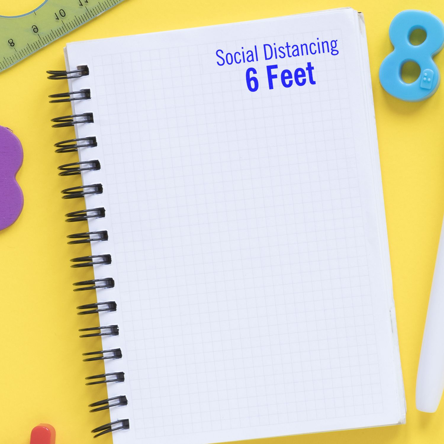 Notebook page with Social Distancing 6 Feet text on a yellow background with school supplies.