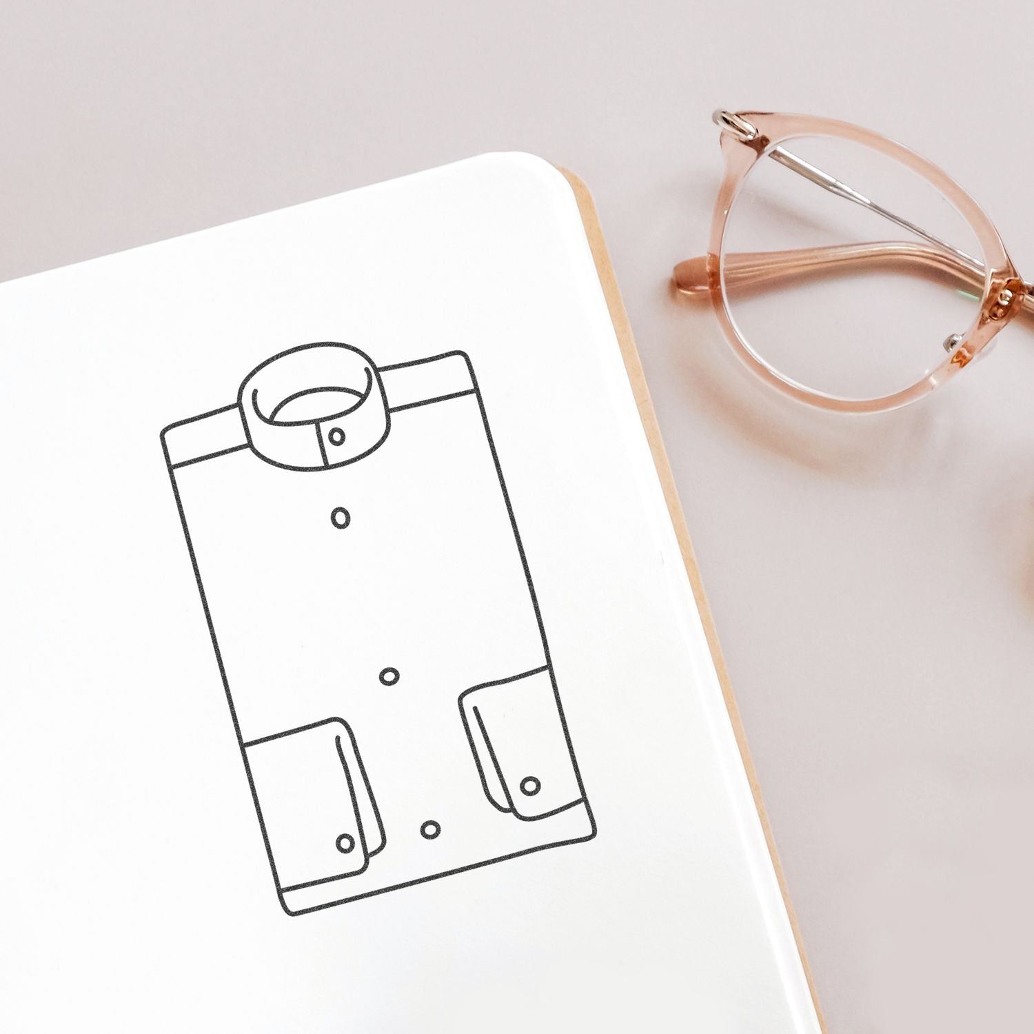 Fashion design sketch notebook with clothing illustration and rose gold eyeglasses on a light desk.