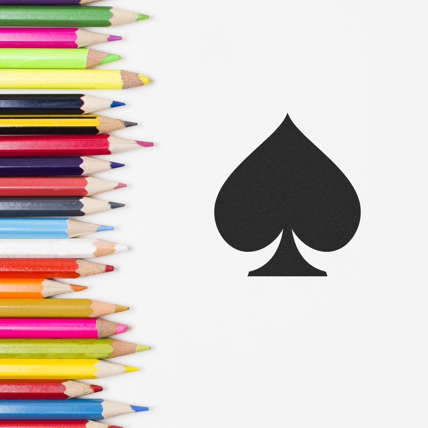 Colorful pencils arranged on white background with black spade symbol, creative art and design concept.