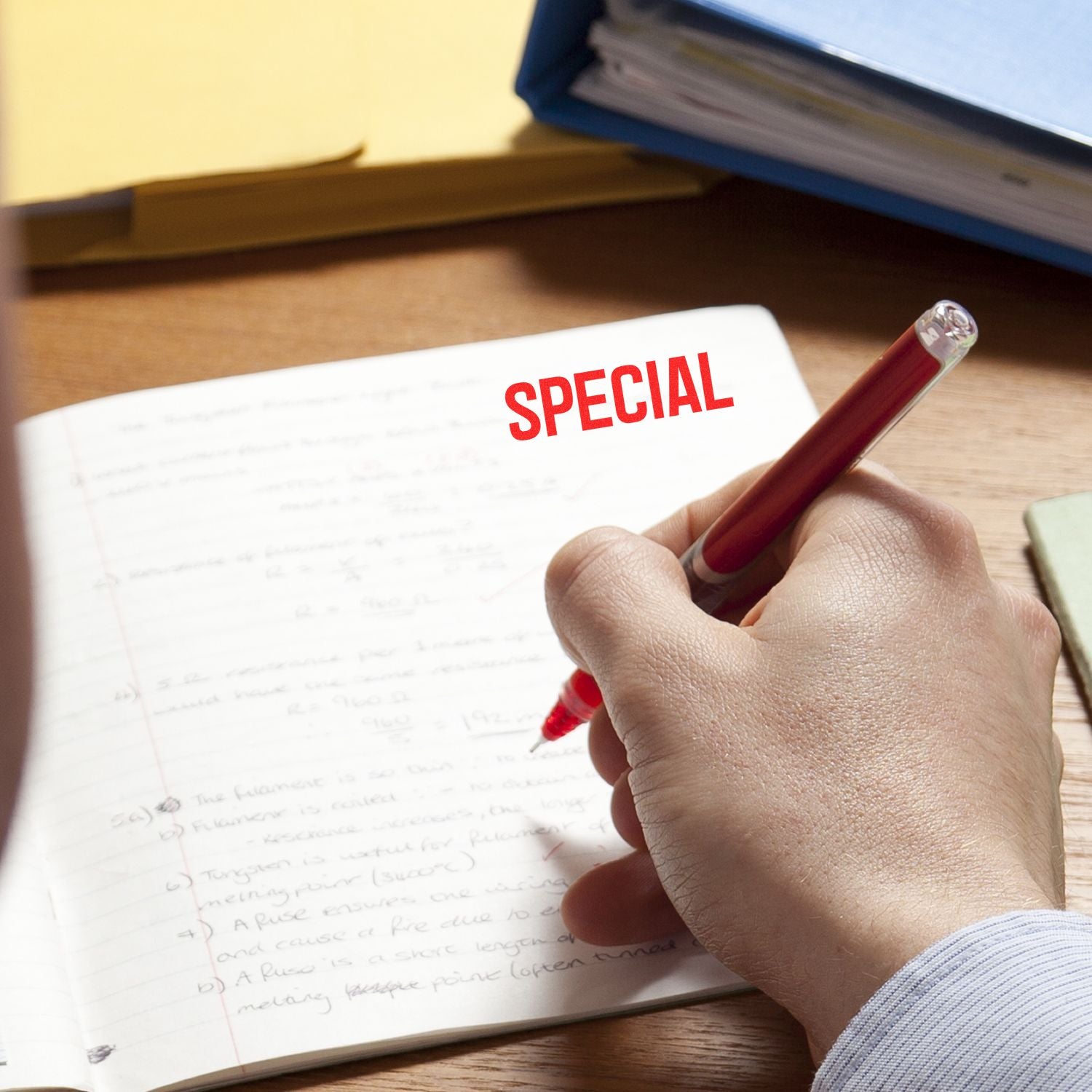 Hand writing in a notebook with red pen and the word SPECIAL on the page, close-up of schoolwork or exam notes.
