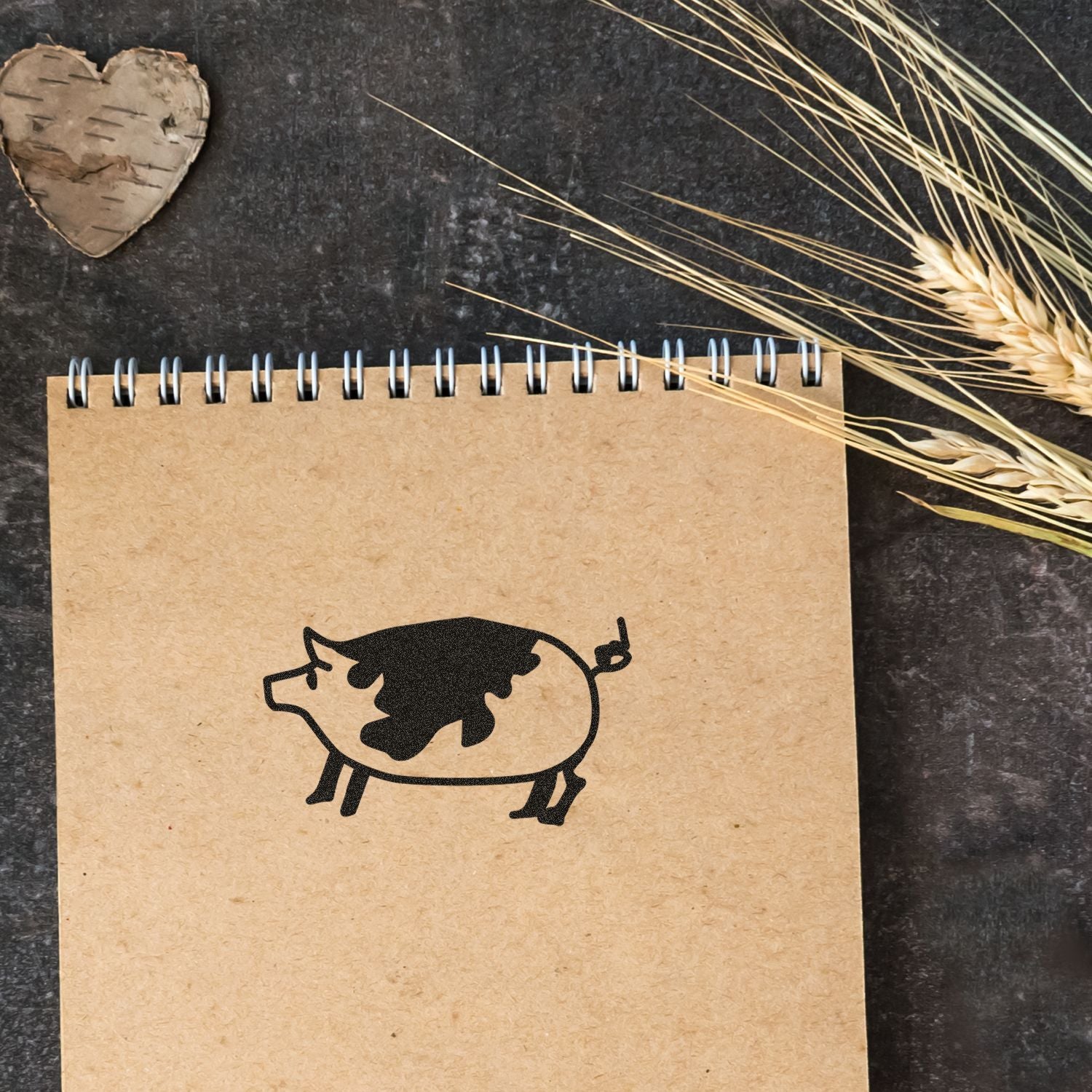 Rustic kraft notebook with black pig illustration on a dark background, styled with dried wheat and a birch heart.