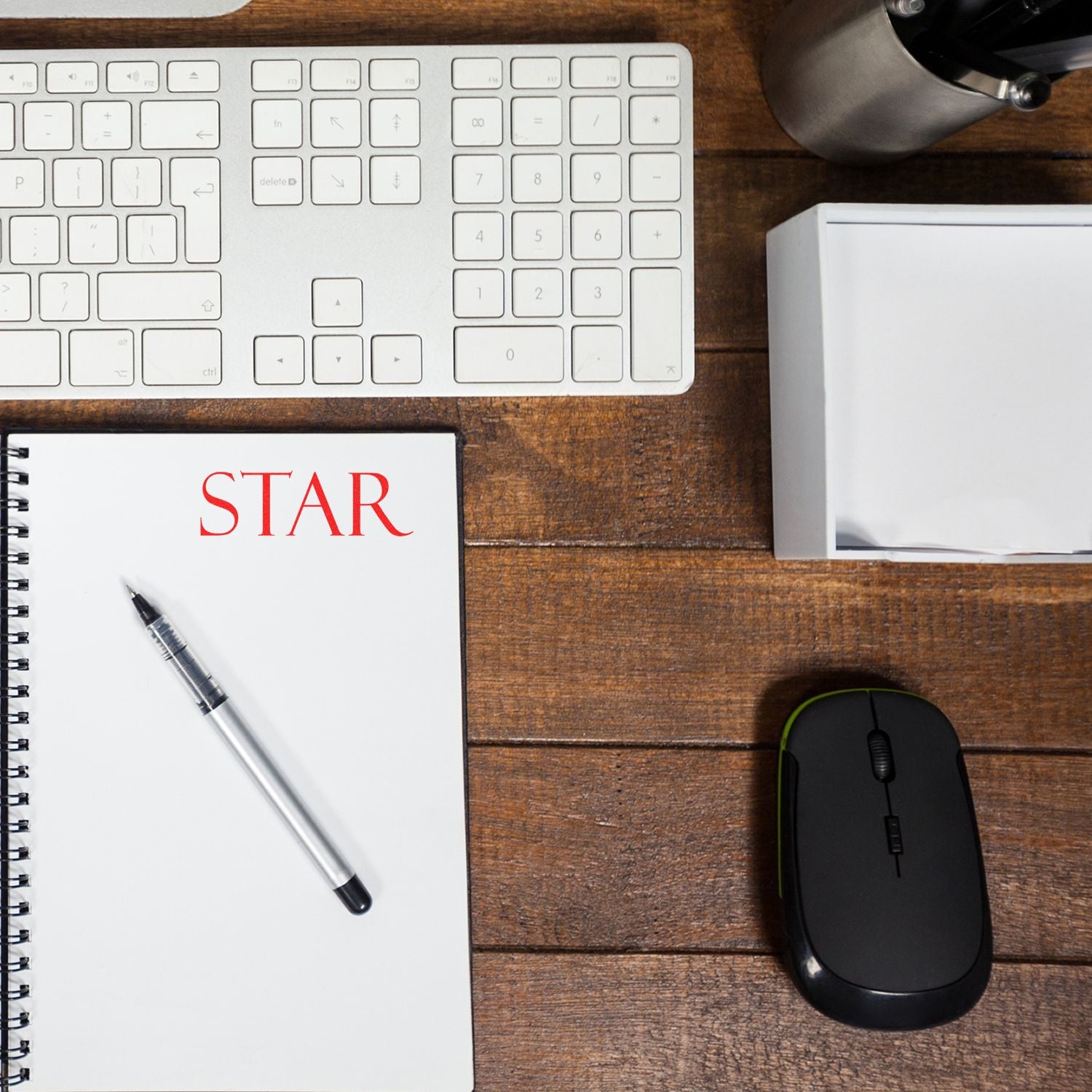 Top view of a modern office desk with keyboard, notebook labeled STAR, pen, mouse, and stationery on a wooden table.