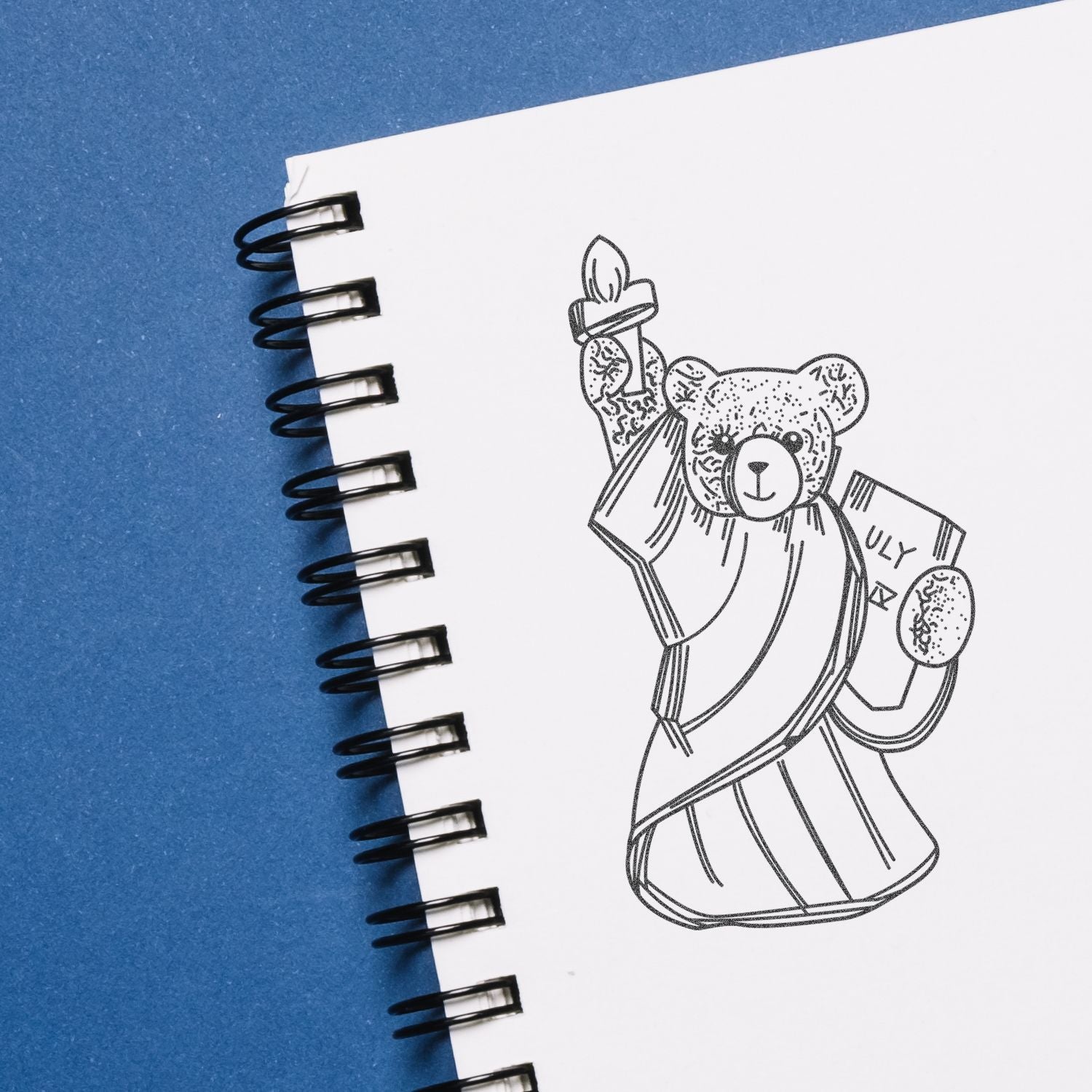 Hand-drawn teddy bear illustration in a spiral notebook on a blue background.