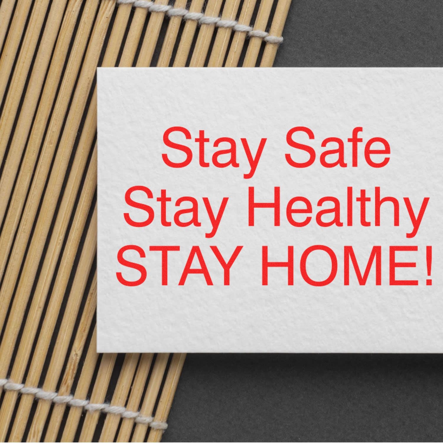 Stay Safe Stay Healthy Stay Home message on a white card with red text on a bamboo mat background.