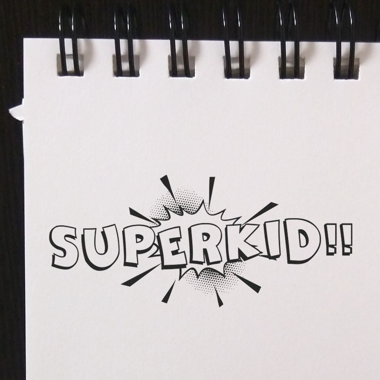Comic-style SUPERKID!! text on a sketchbook page with bold black lettering and burst graphic.