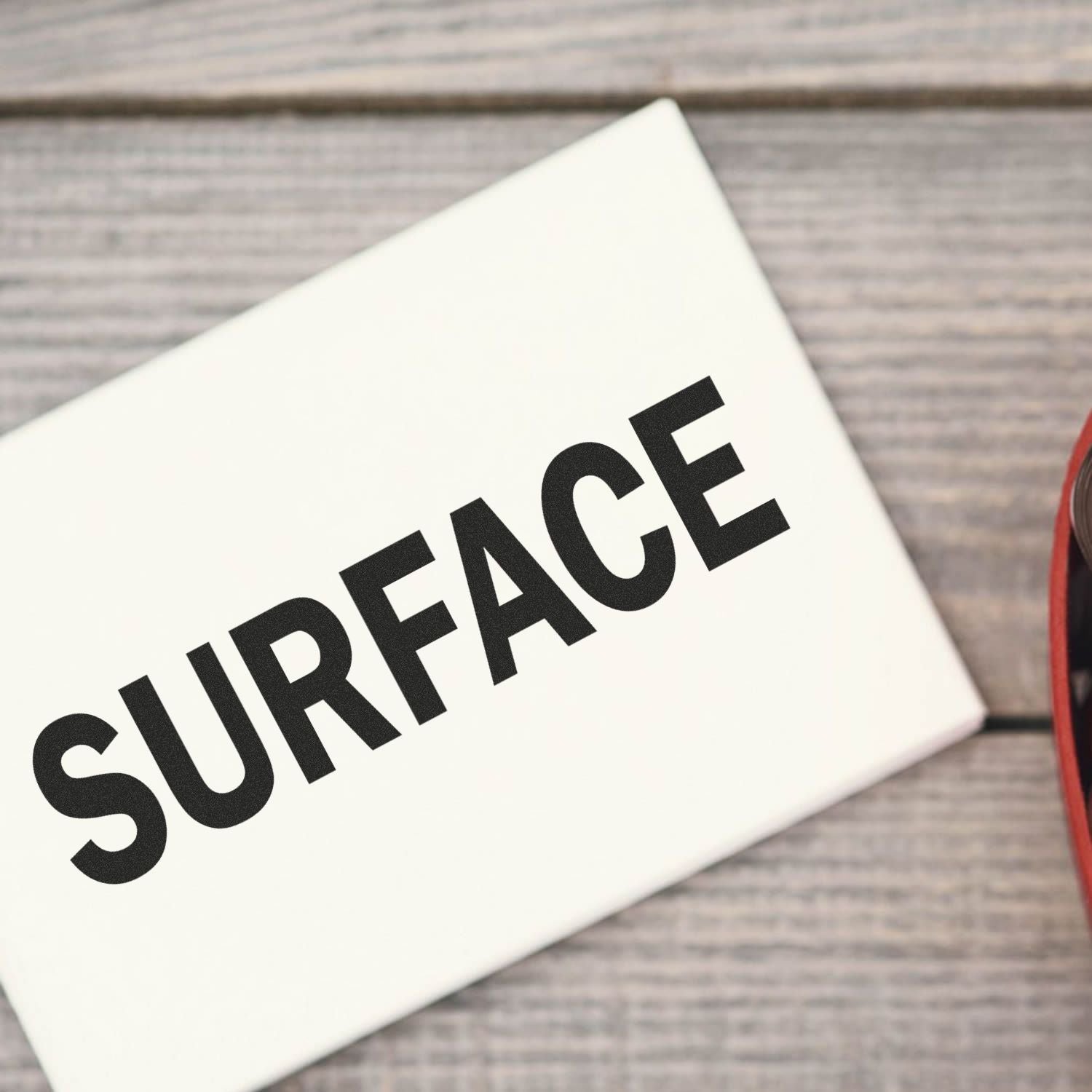 Close-up of a white card on a wooden table with bold text SURFACE, illustrating surface finishing and cleaning services.