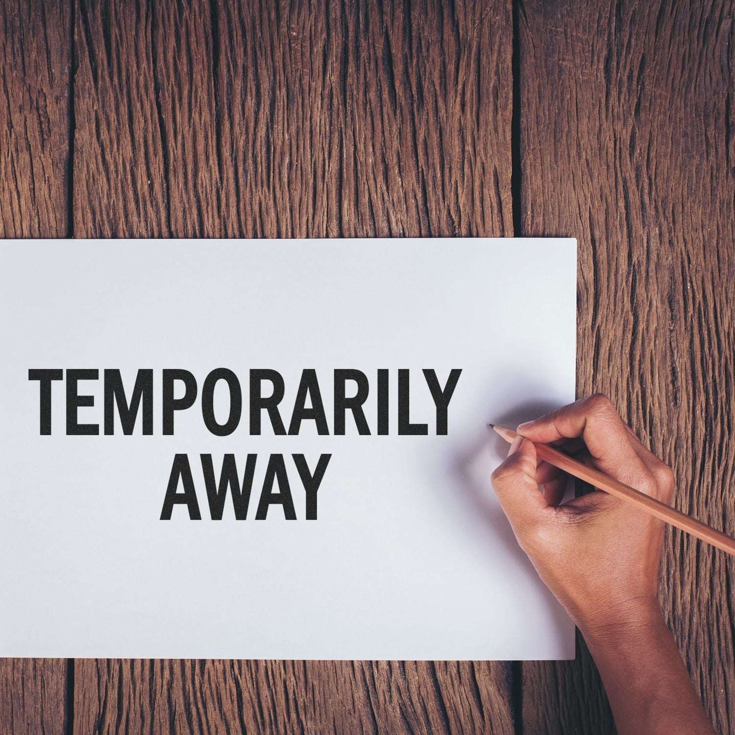 Hand writing Temporarily Away on a note, conveying temporary absence and an out-of-office message.