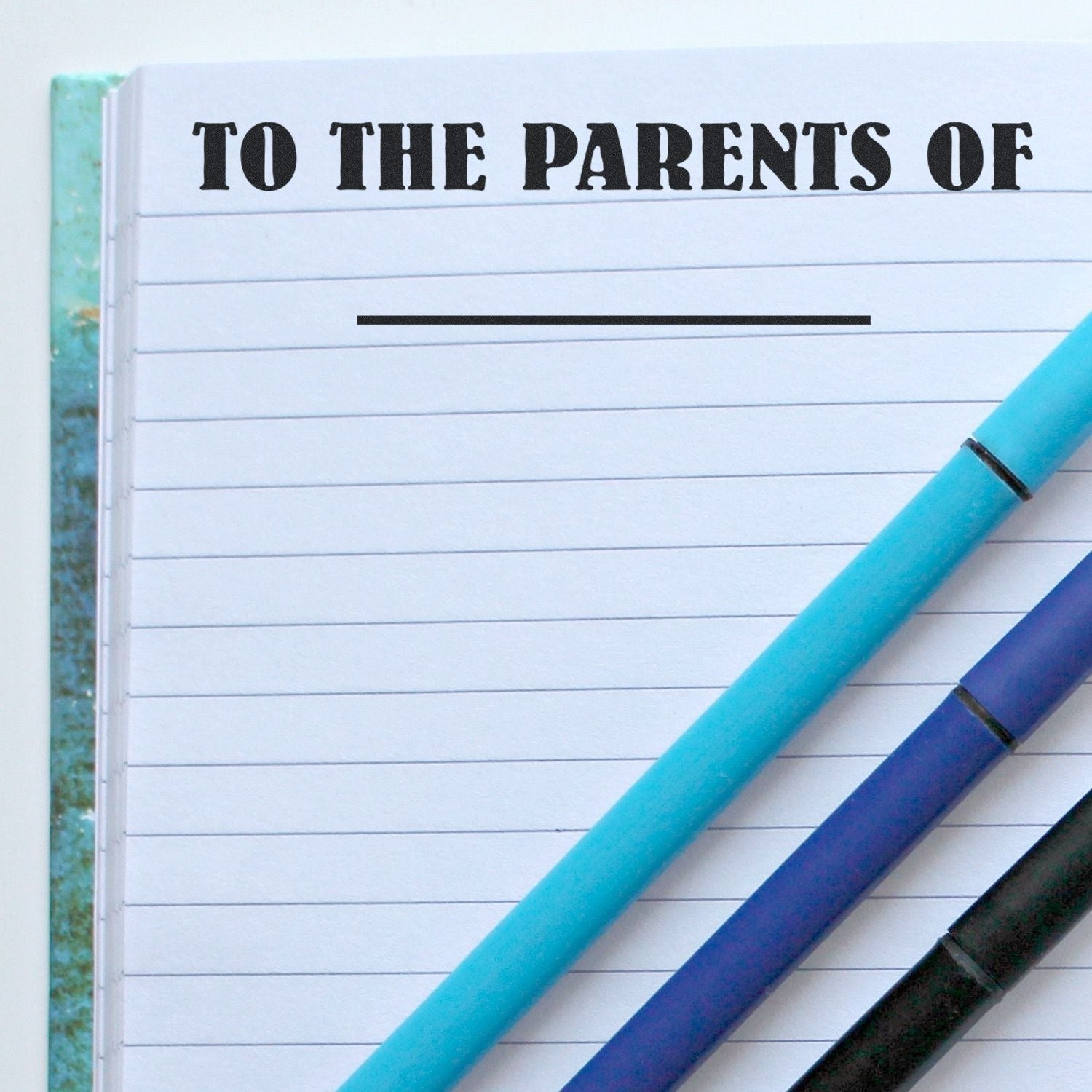 Close-up of lined notebook page with To the parents of heading and colorful pens, ideal for back-to-school planning.