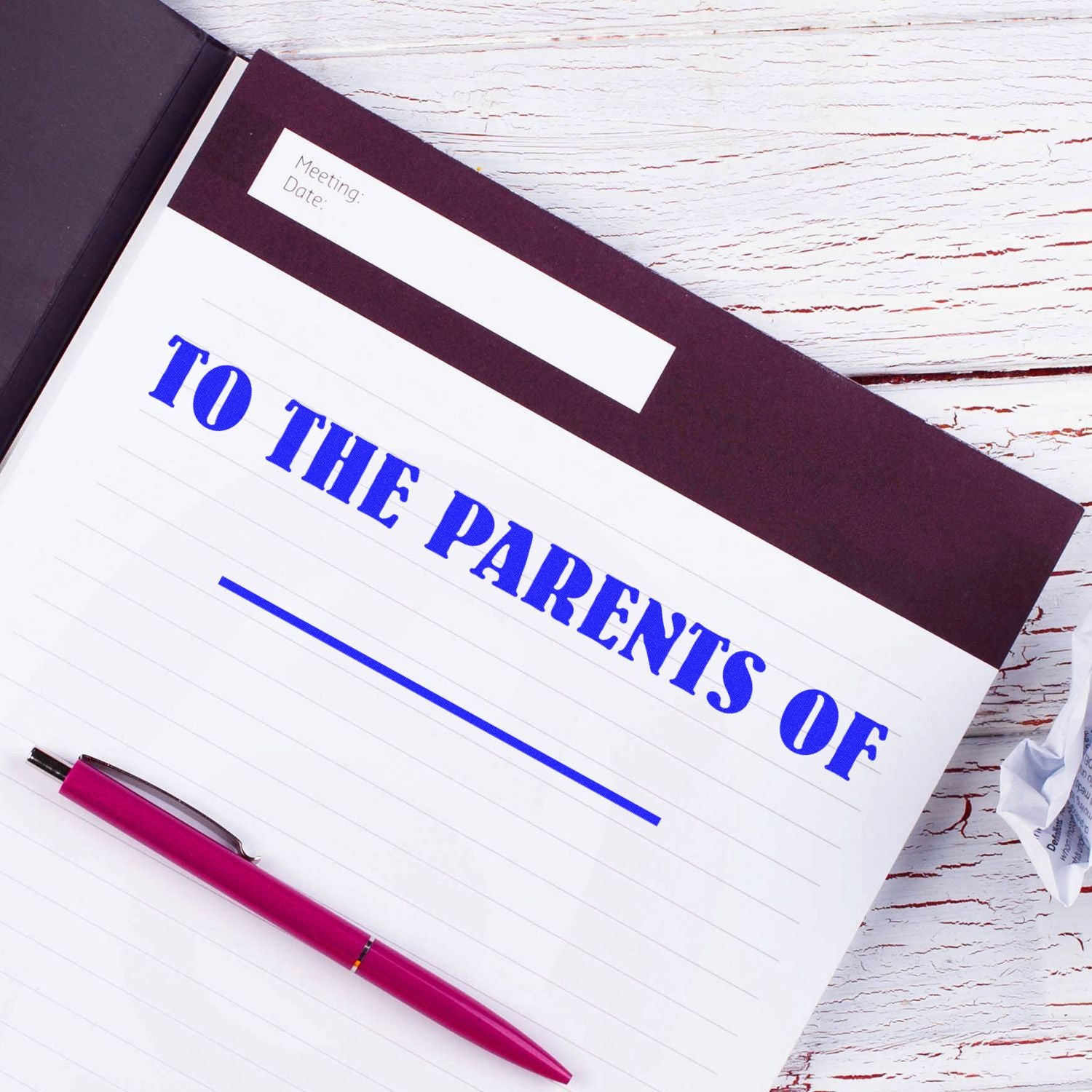 Open notebook labeled To the Parents Of with pen on a white wooden desk, parent communication folder for teachers and school meetings.
