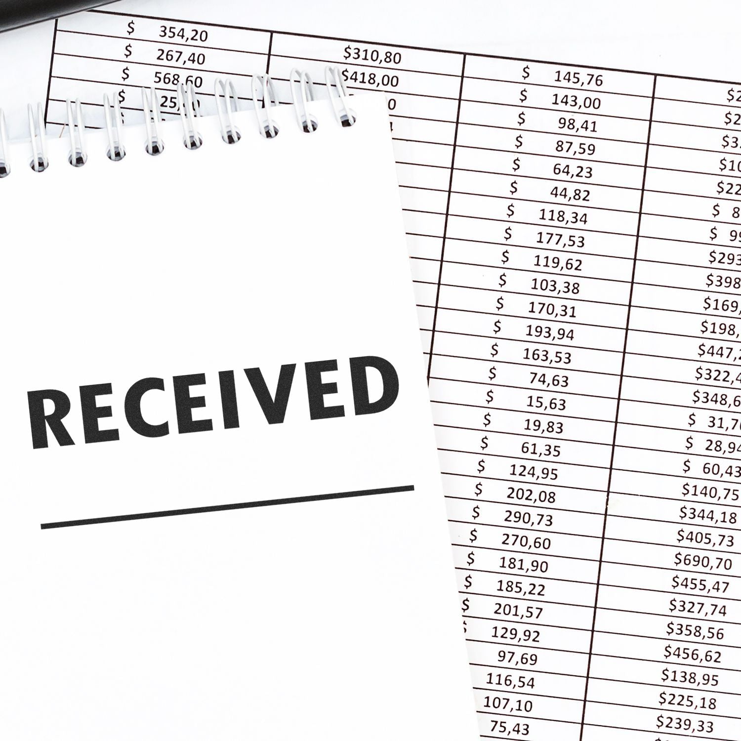 Blank spiral notebook with RECEIVED stamped on top of an accounting spreadsheet with dollar amounts and financial records.