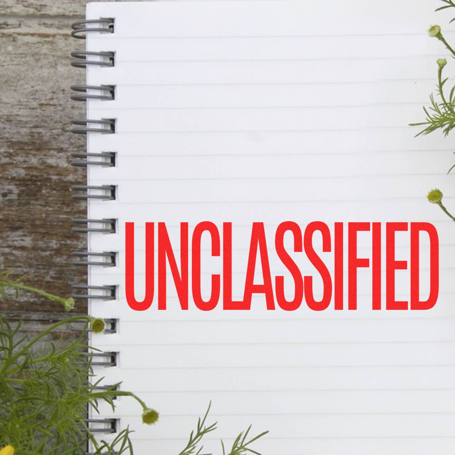 Blank spiral notebook page with bold red UNCLASSIFIED text on a rustic wooden background with green plant accents.