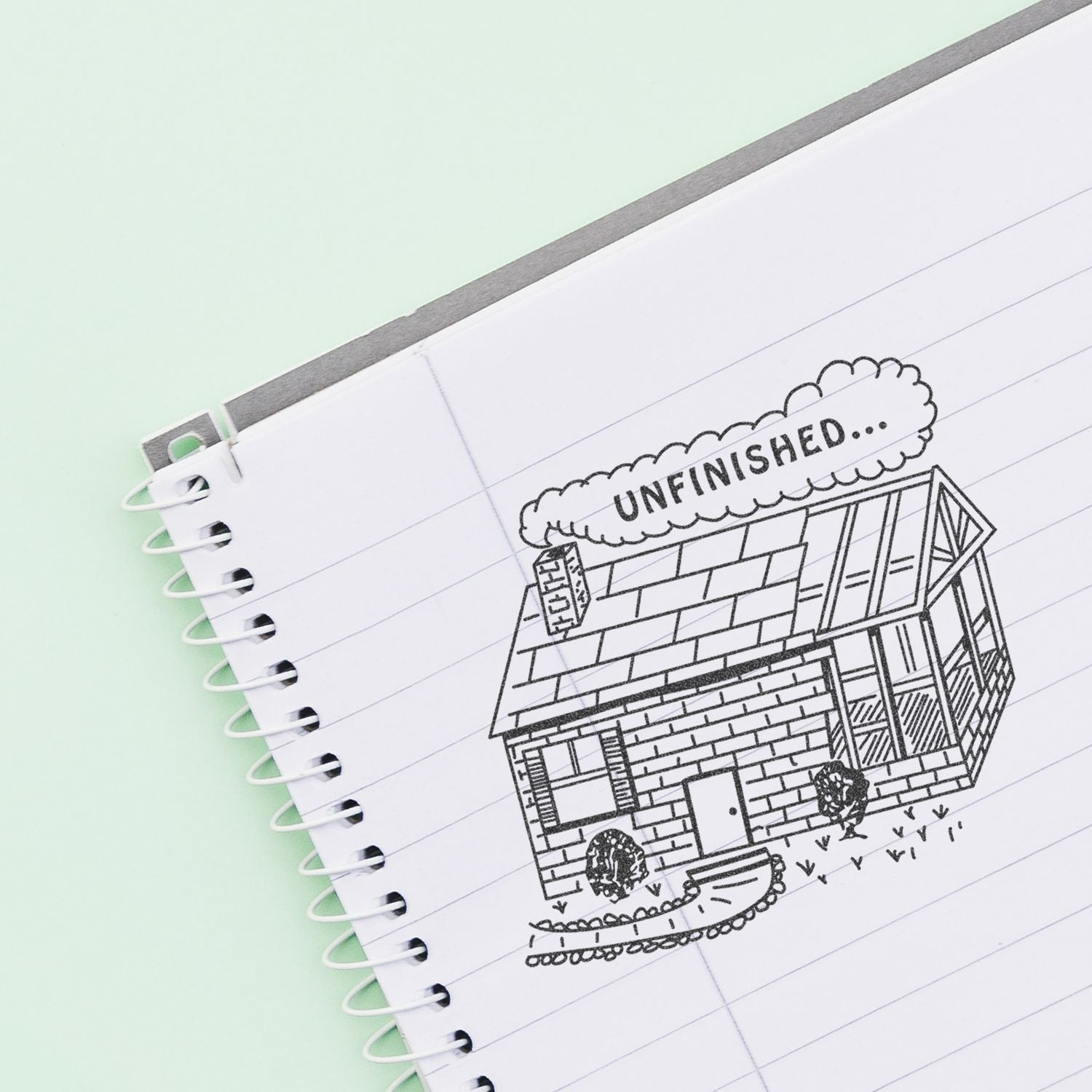 Unfinished house sketch on spiral notebook page with UNFINISHED text, creative home design concept.
