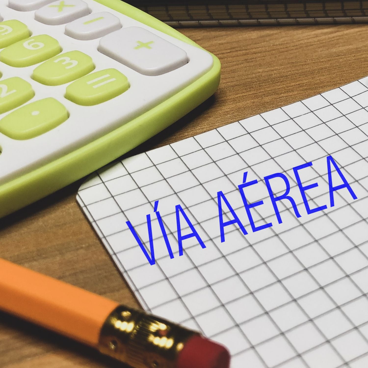 Calculadora, lpiz y cuaderno cuadriculado con texto Va area sobre escritorio de madera.