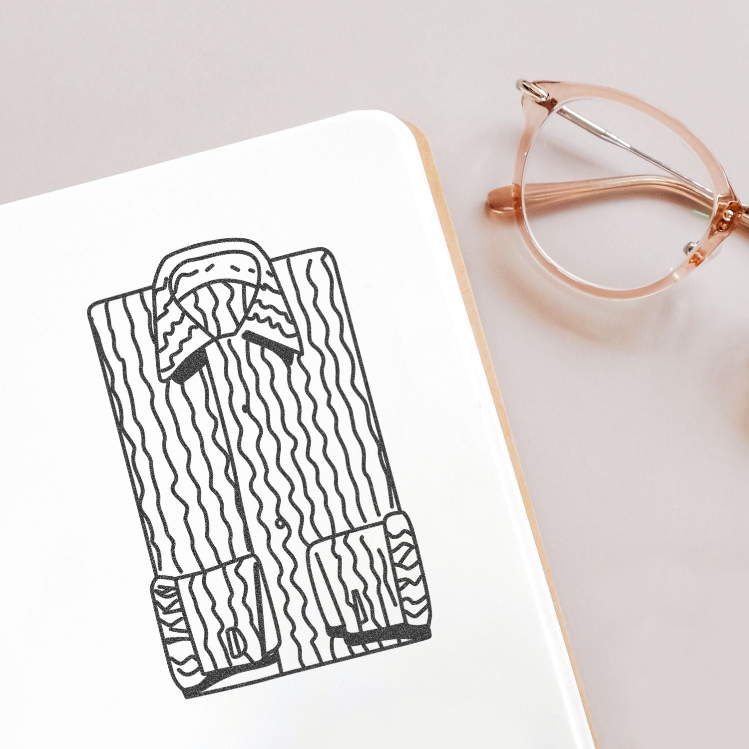 Minimalist notebook with fashion sketch of a striped shirt and rose gold eyeglasses on a clean desk