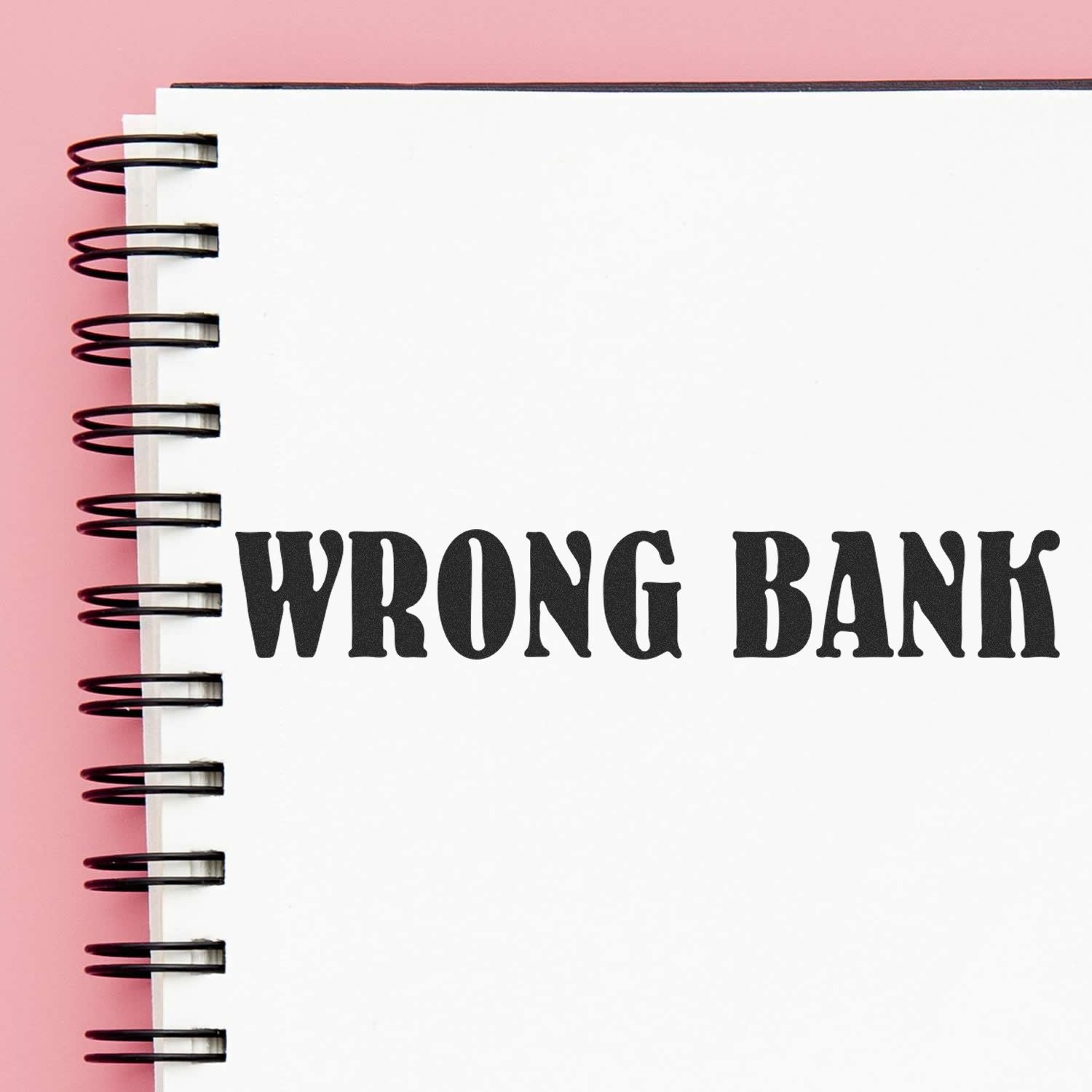 Close-up of a spiral notebook with WRONG BANK text on a pink background.