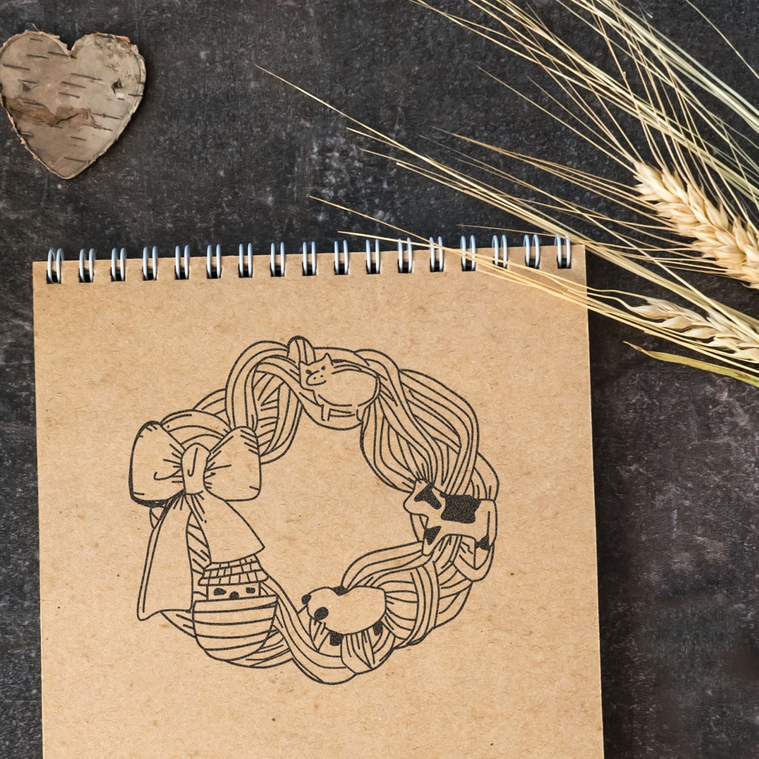 Kraft spiral notebook with cute hand-drawn farm animal wreath illustration on a rustic dark background with wheat decor.