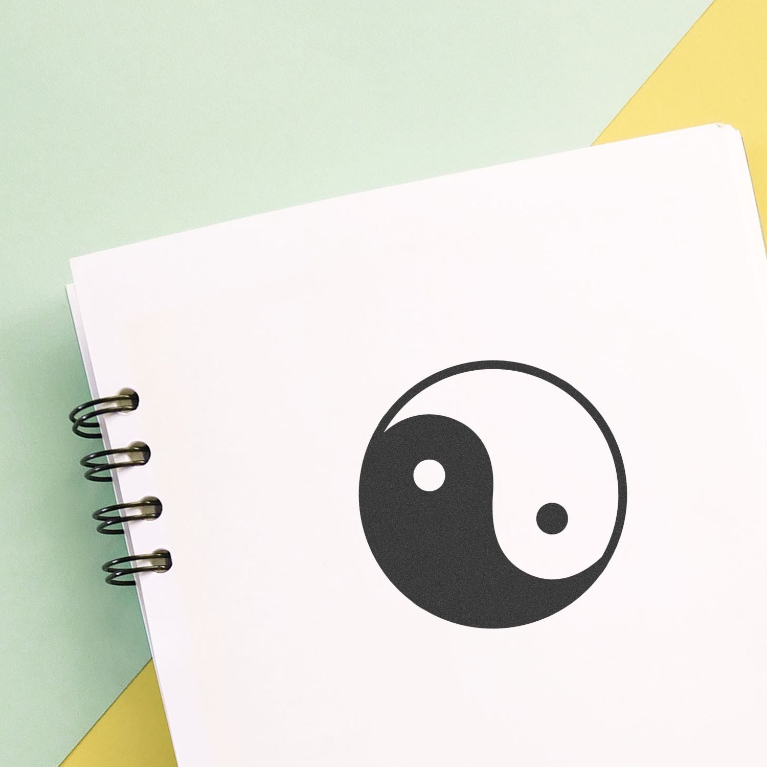 Spiral notebook page with yin yang symbol on a pastel green and yellow background.
