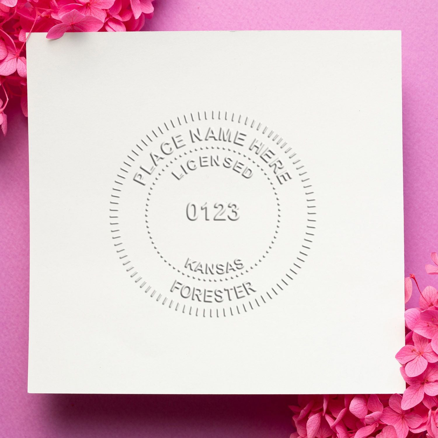 Embossed white invitation card with placeholder text, centered circular seal, and pink flowers on a soft pink background