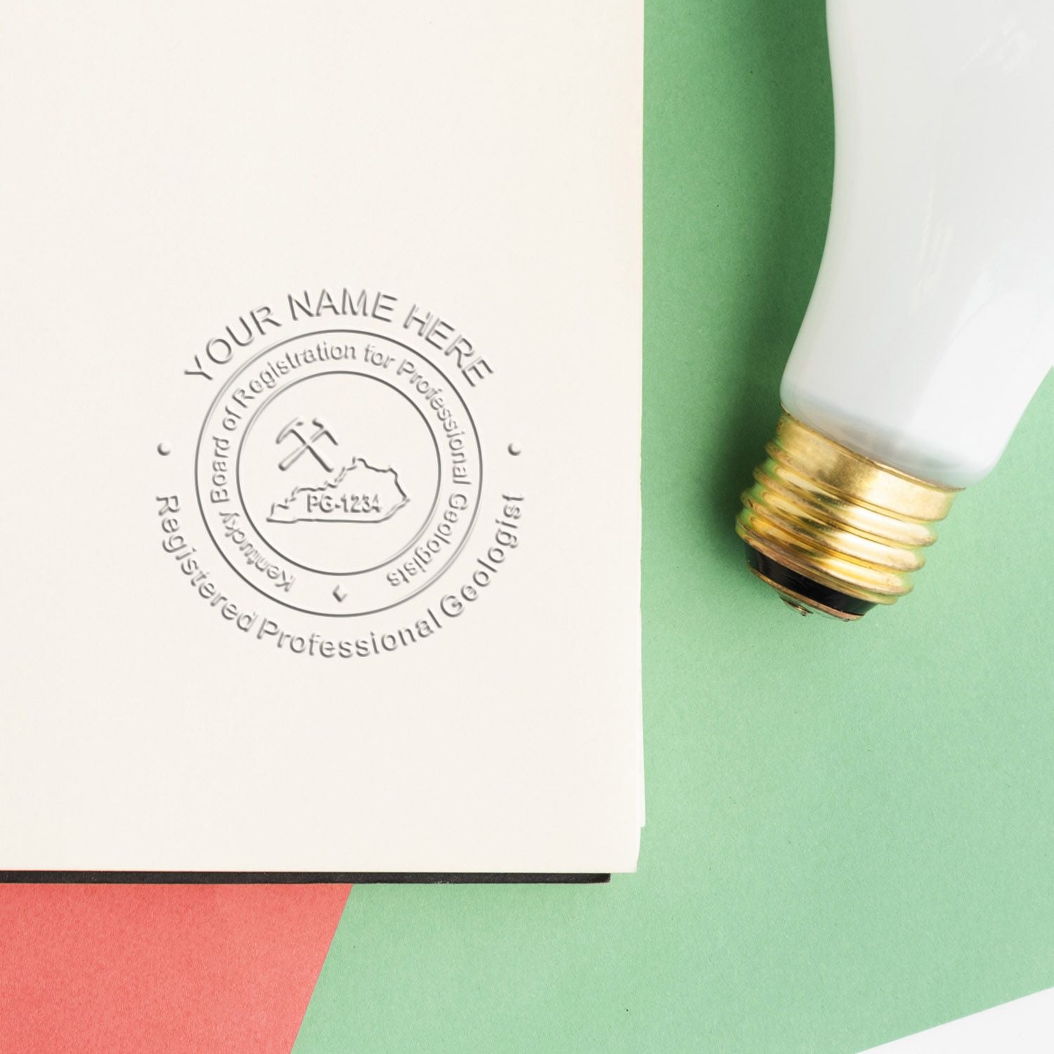 Custom embossed logo stamp on a white business card mockup beside a vintage light bulb on a green pastel background.