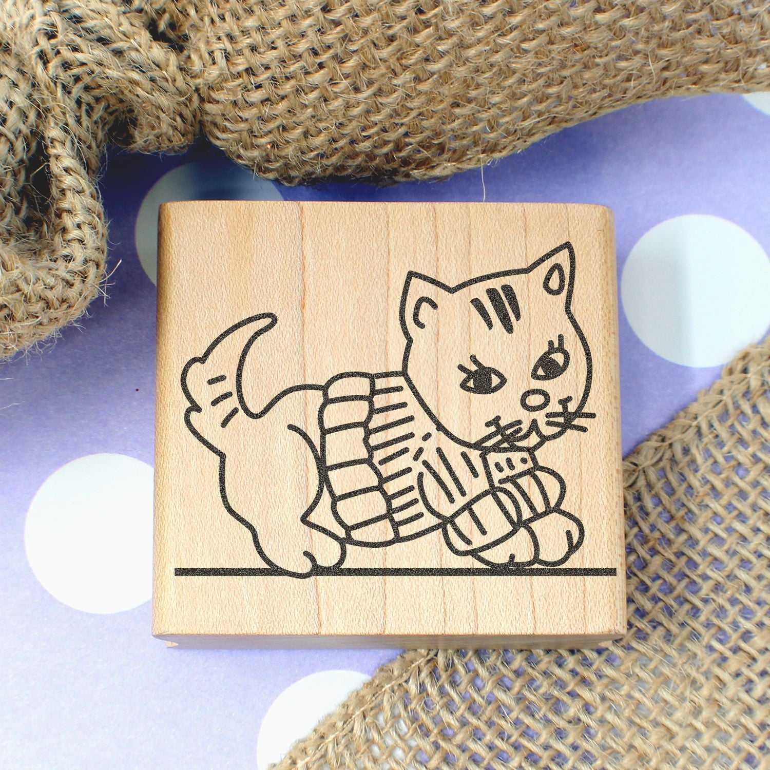 Wooden cat stamp with cute kitten outline on burlap and purple polka dot background, ideal for craft and DIY projects.