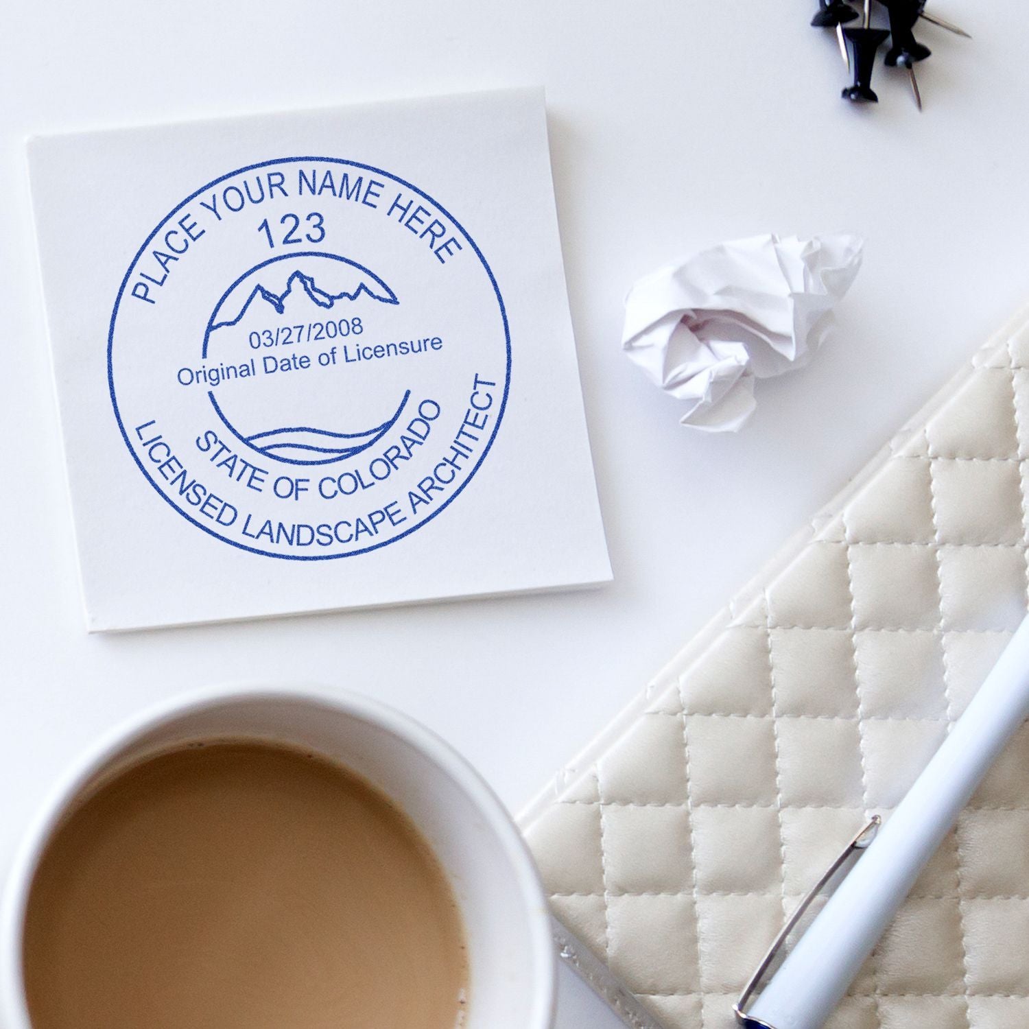 Licensed landscape architect stamp on notebook with coffee cup, pen, and crumpled paper on a clean white desk workspace