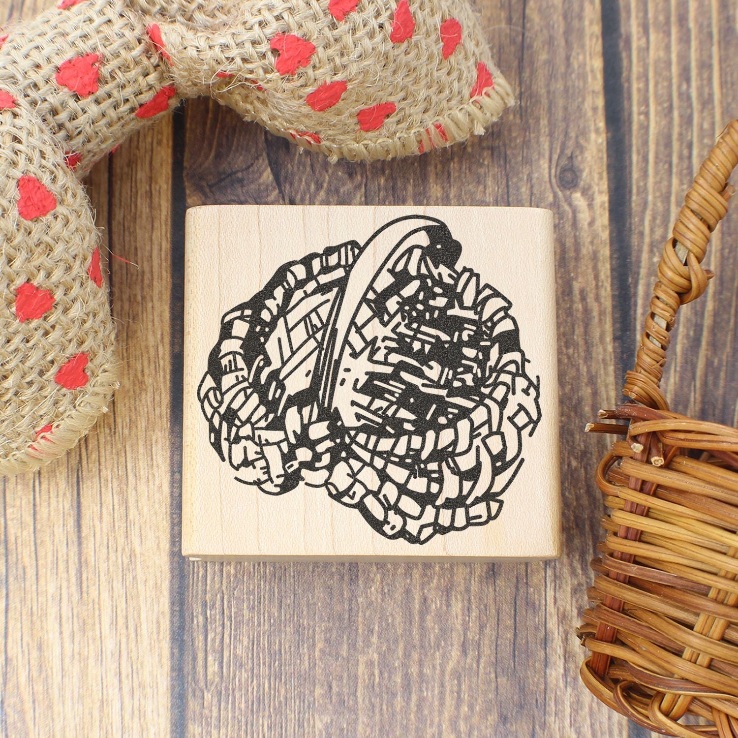 Wooden rubber stamp with woven basket design on rustic wood background, surrounded by burlap and wicker decor.