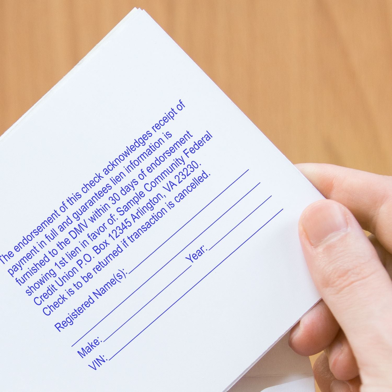 Hand holds a sample DMV check receipt form showing credit union address, VIN, and check cancellation notice.