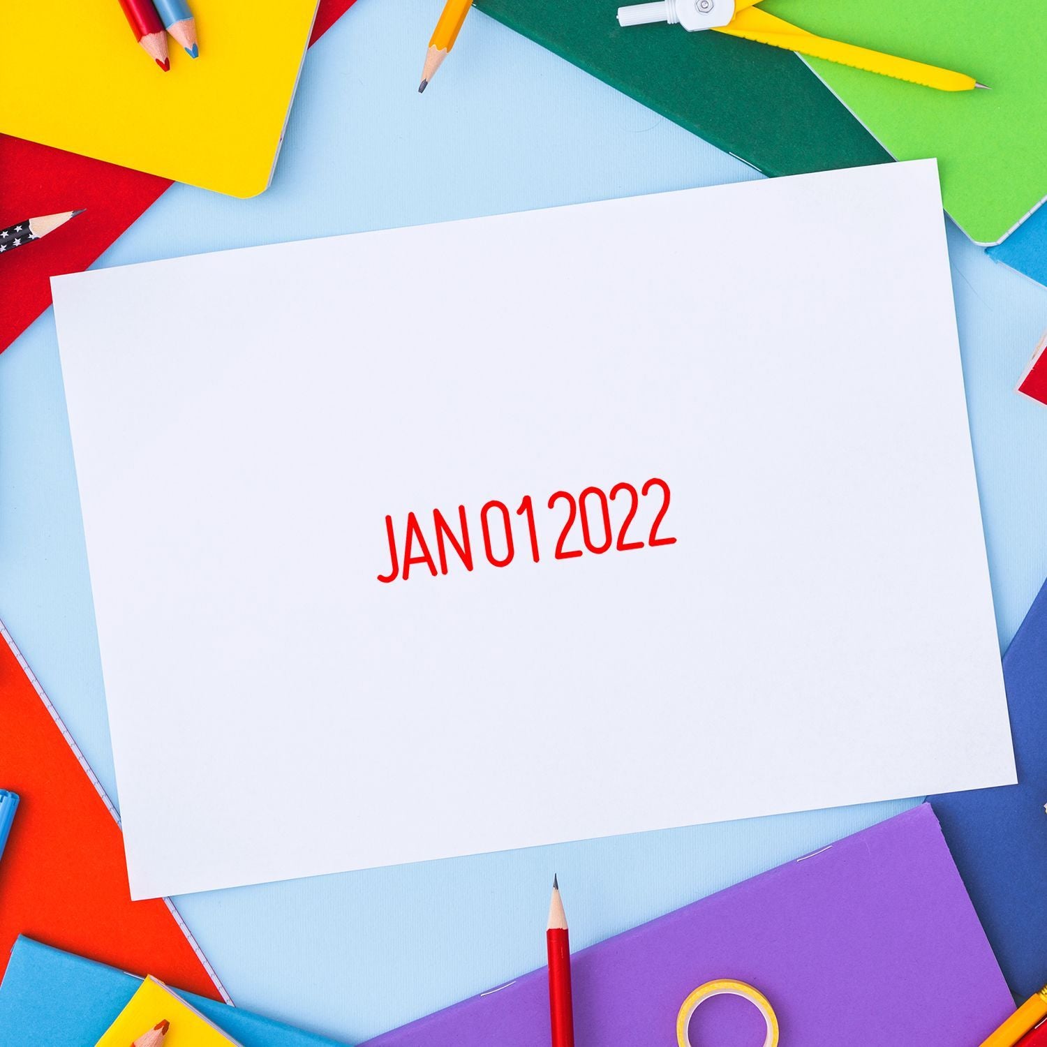 Blank white paper with red JAN012022 text surrounded by colorful pencils, notebooks, and school supplies on a blue background.