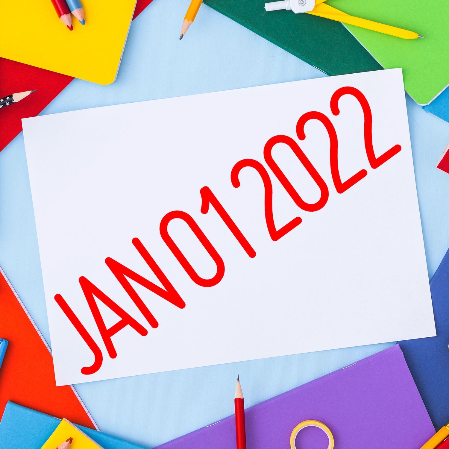 JAN 2022 text on white paper surrounded by colorful notebooks and pencils, creative calendar concept.