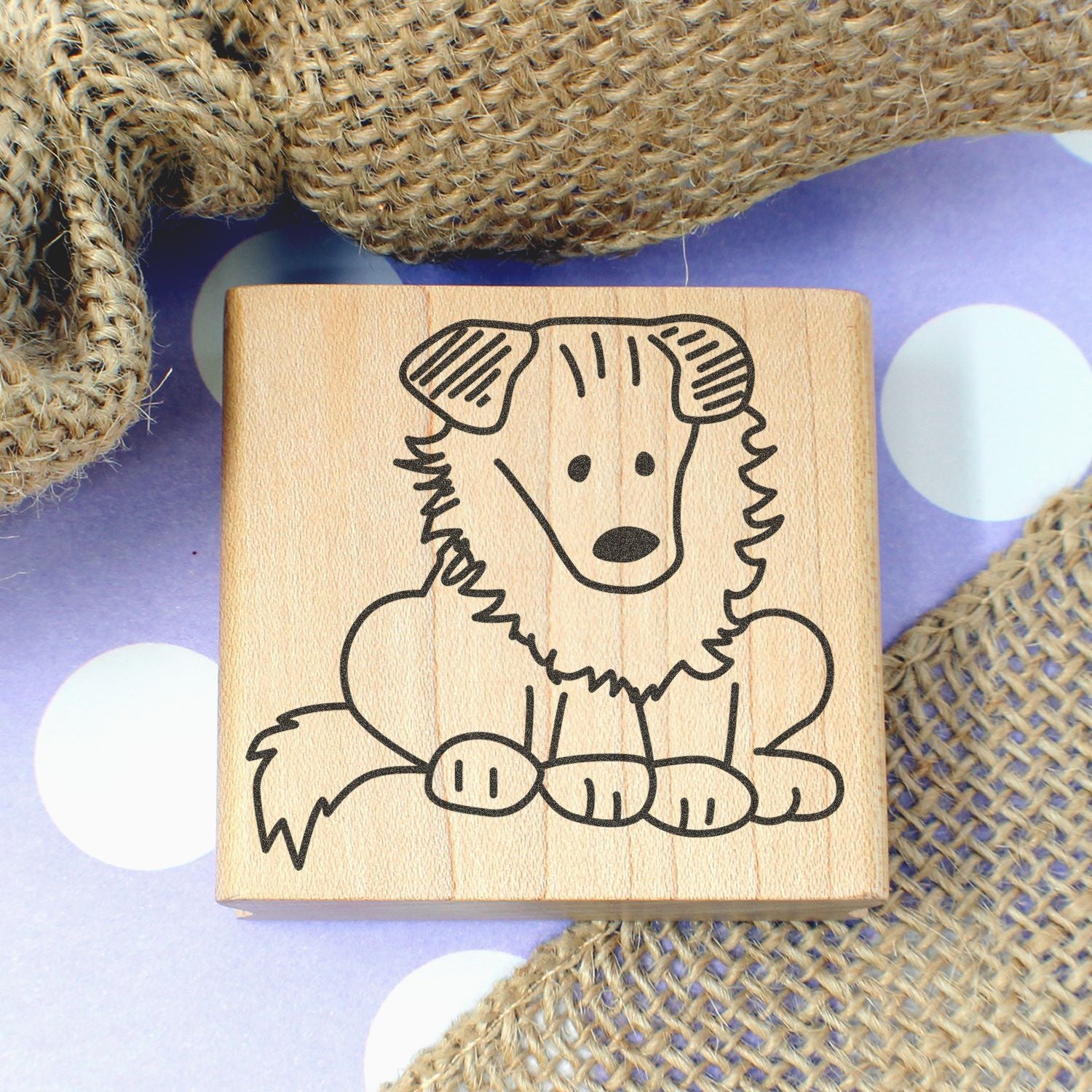 Cute wooden dog stamp with simple black line art, styled on burlap fabric and a purple polka dot background.