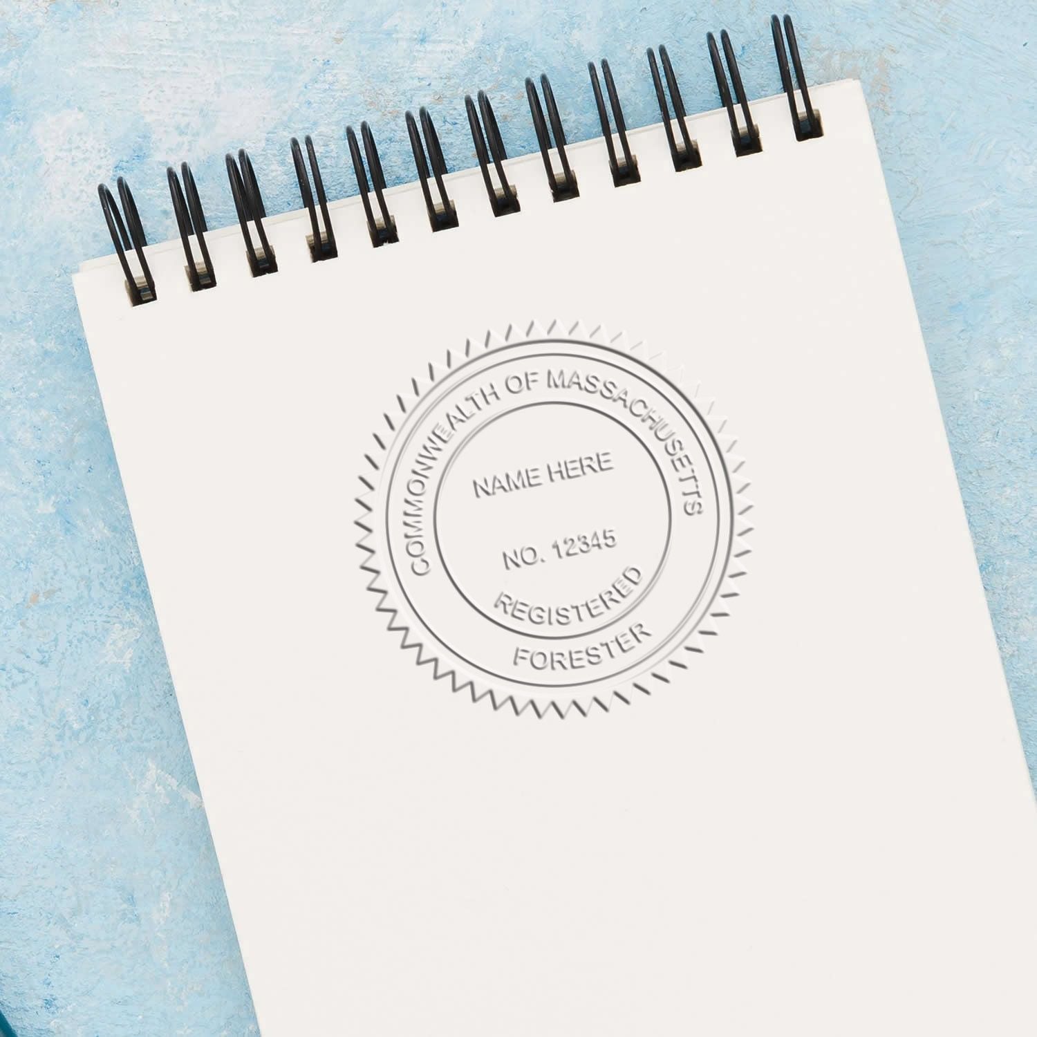Blank spiral notebook with Commonwealth of Massachusetts Registered Forester seal stamp on blue background