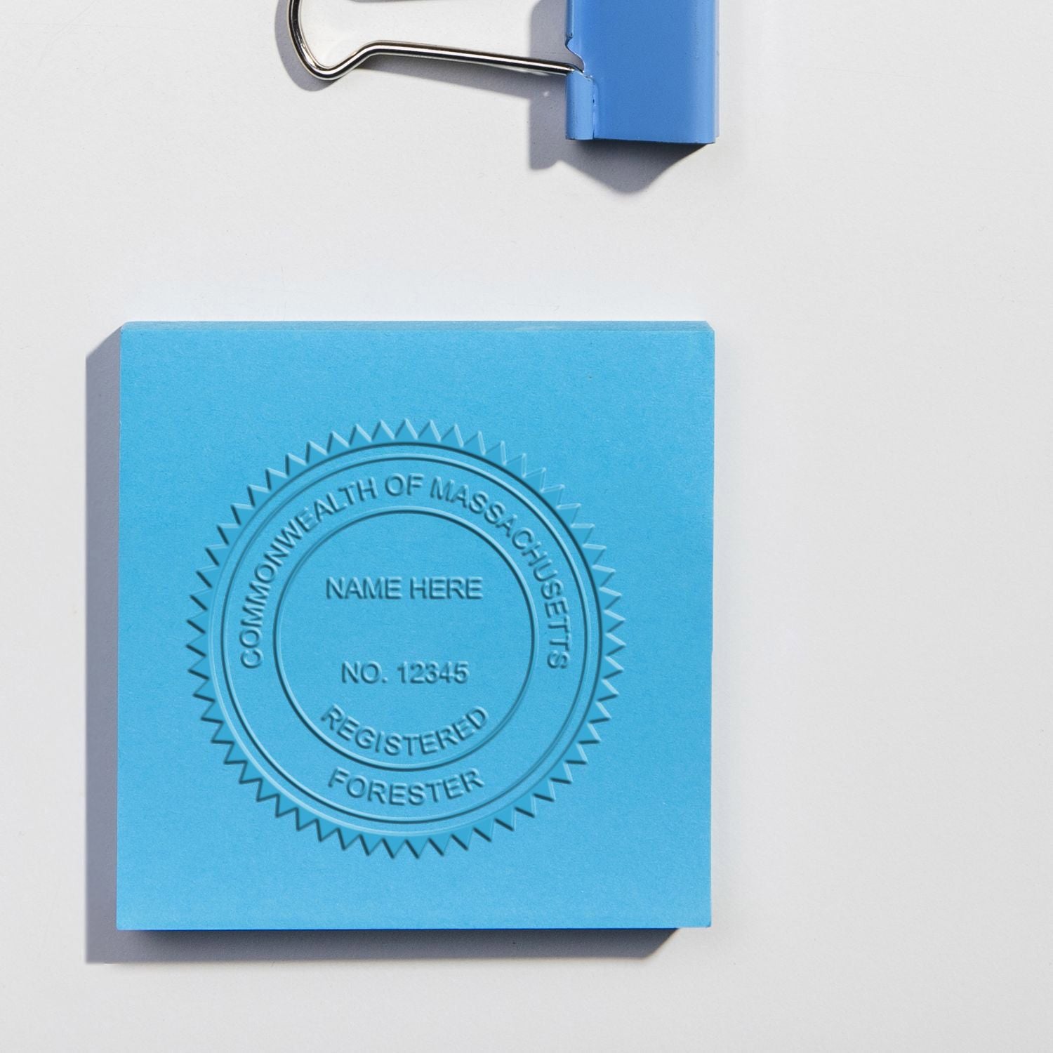 Blue embossed Commonwealth of Massachusetts Registered Forester seal on paper with a binder clip visible above.