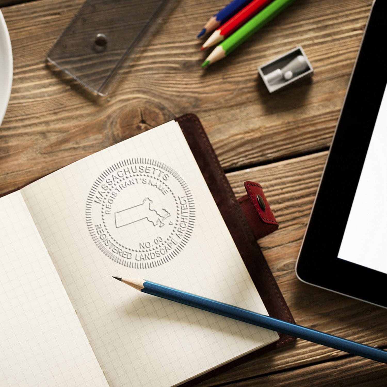 Notebook with Massachusetts registered landscape architect seal, pencils, and tablet on a wooden desk