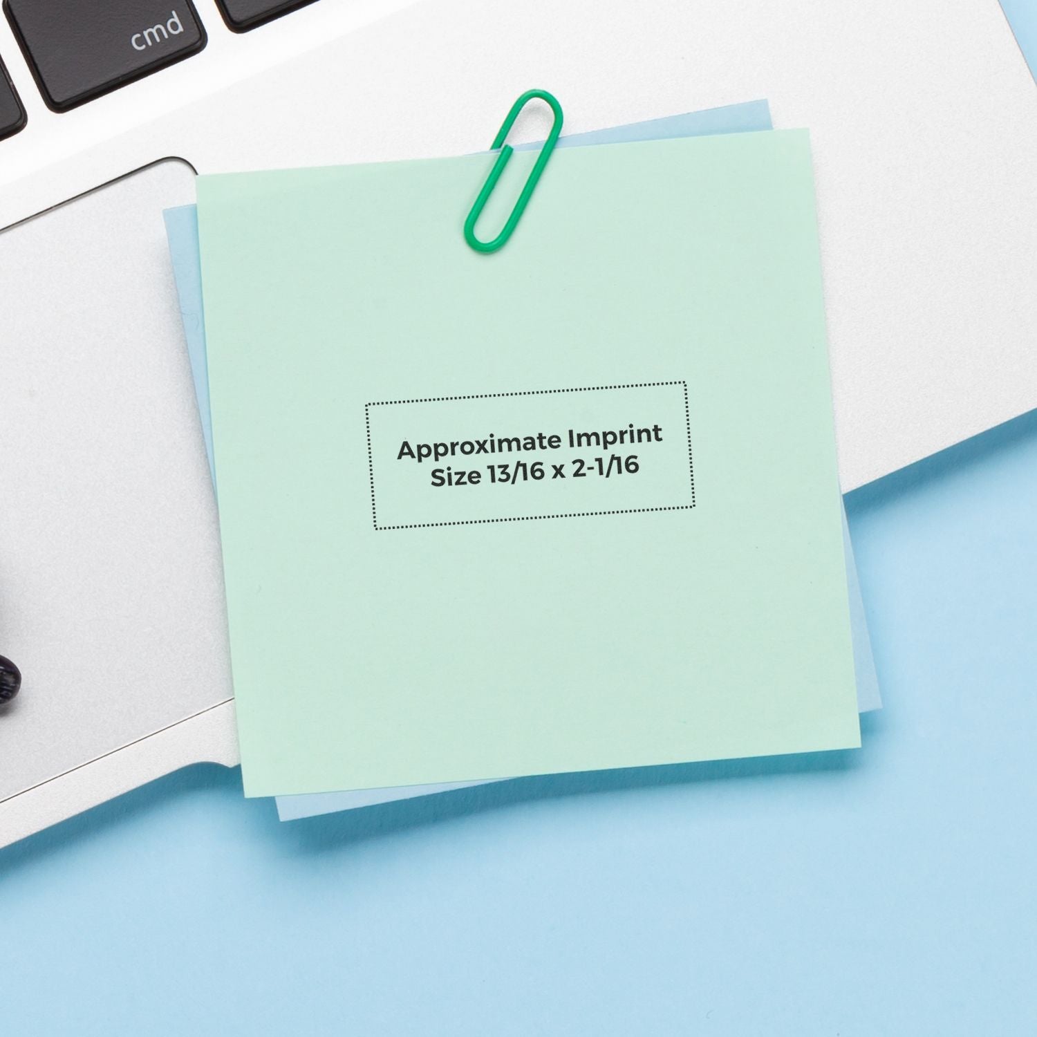 Mint green sticky note with paper clip on laptop keyboard, featuring approximate imprint size text on a clean office desk background.