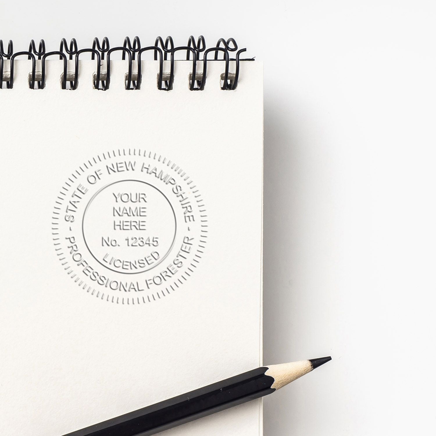 Blank spiral notebook with embossed State of New Hampshire Professional Forester license seal and pencil on white background