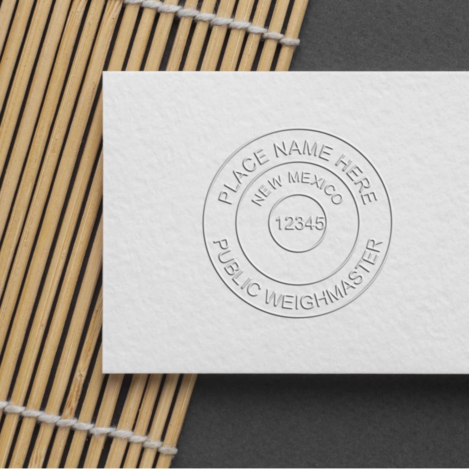 Embossed business card mockup with circular Public Weighmaster logo on a white card over a bamboo mat background.