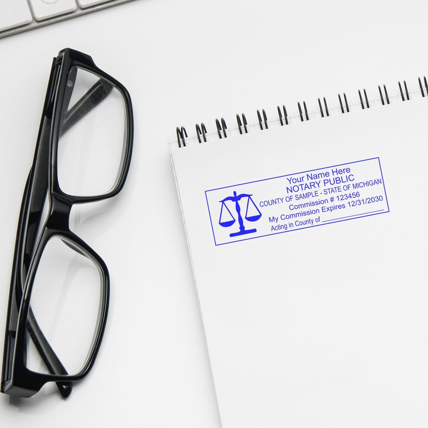 Black eyeglasses beside a notary public stamp on a white office desk with a spiral notebook.
